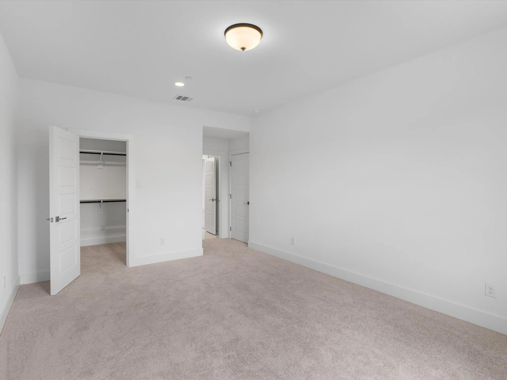 Carpeted room with white walls, a walk-in closet, and a semi-flush mount ceiling light
