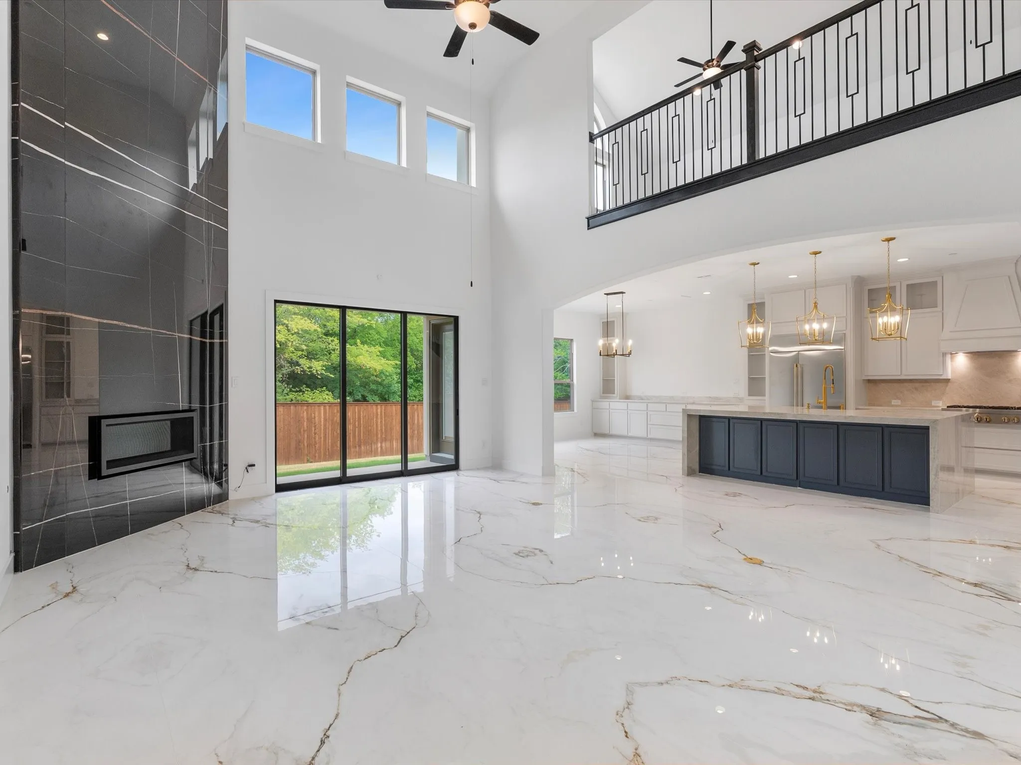 Soaring ceilings with upper windows, a contemporary fireplace, and a second-story balcony featuring a decorative metal railing