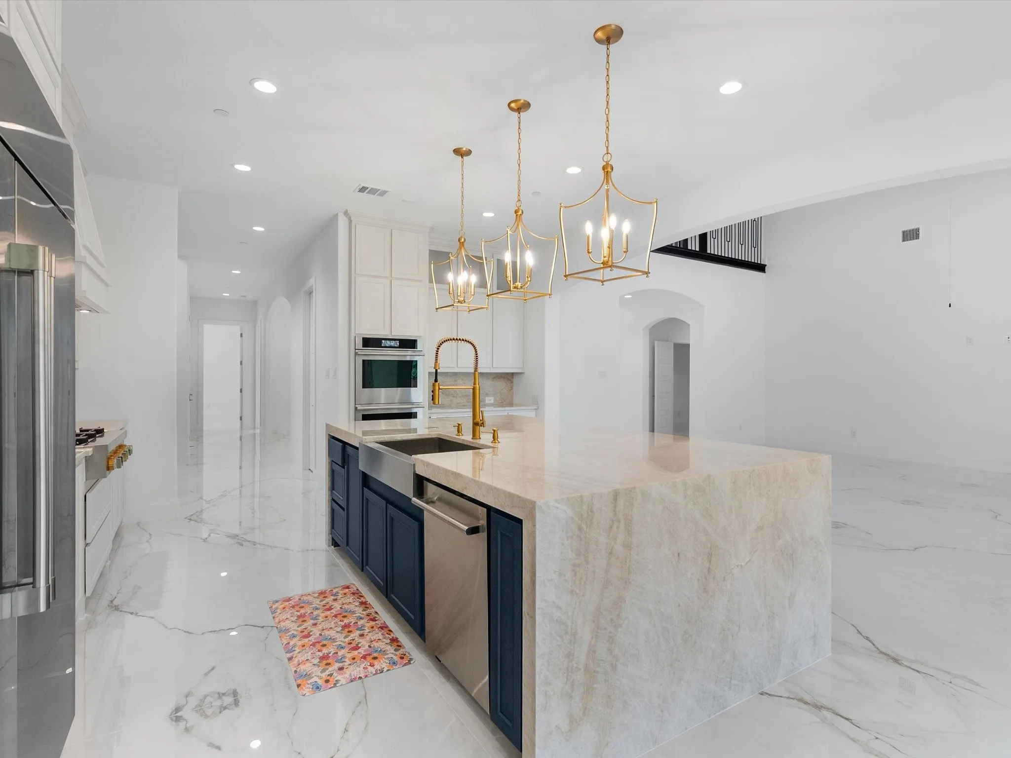 Gourmet kitchen with a large island featuring a waterfall countertop, farmhouse sink, gold-toned fixtures, stainless steel appliances, and recessed lighting