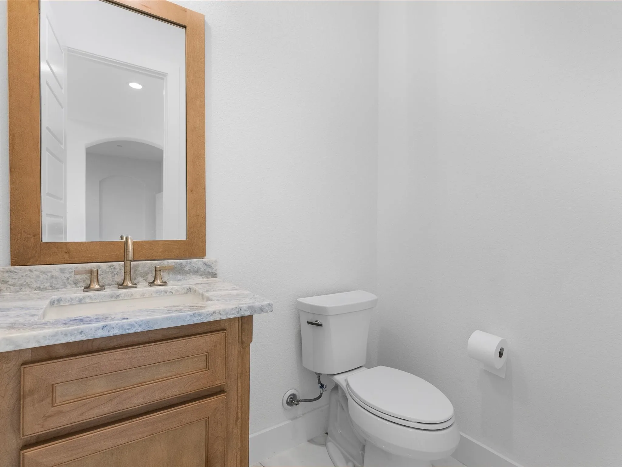 Light wood-finish vanity with an undermount sink, multi-tone countertop, and a bronze-finish faucet