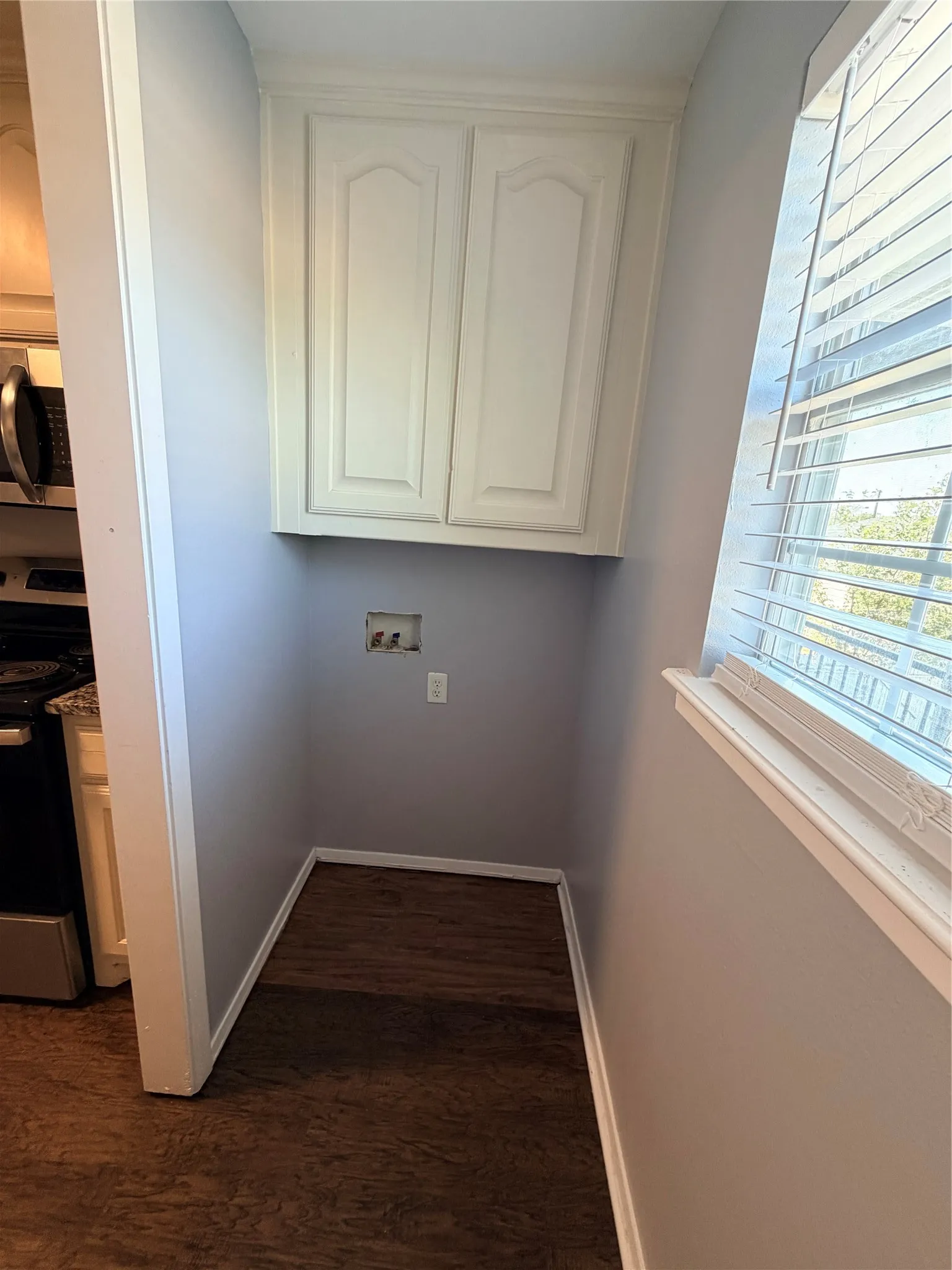 Full size washer & dryer hook up with Built-in wall cabinetry, wood-finish flooring, and a large window with blinds