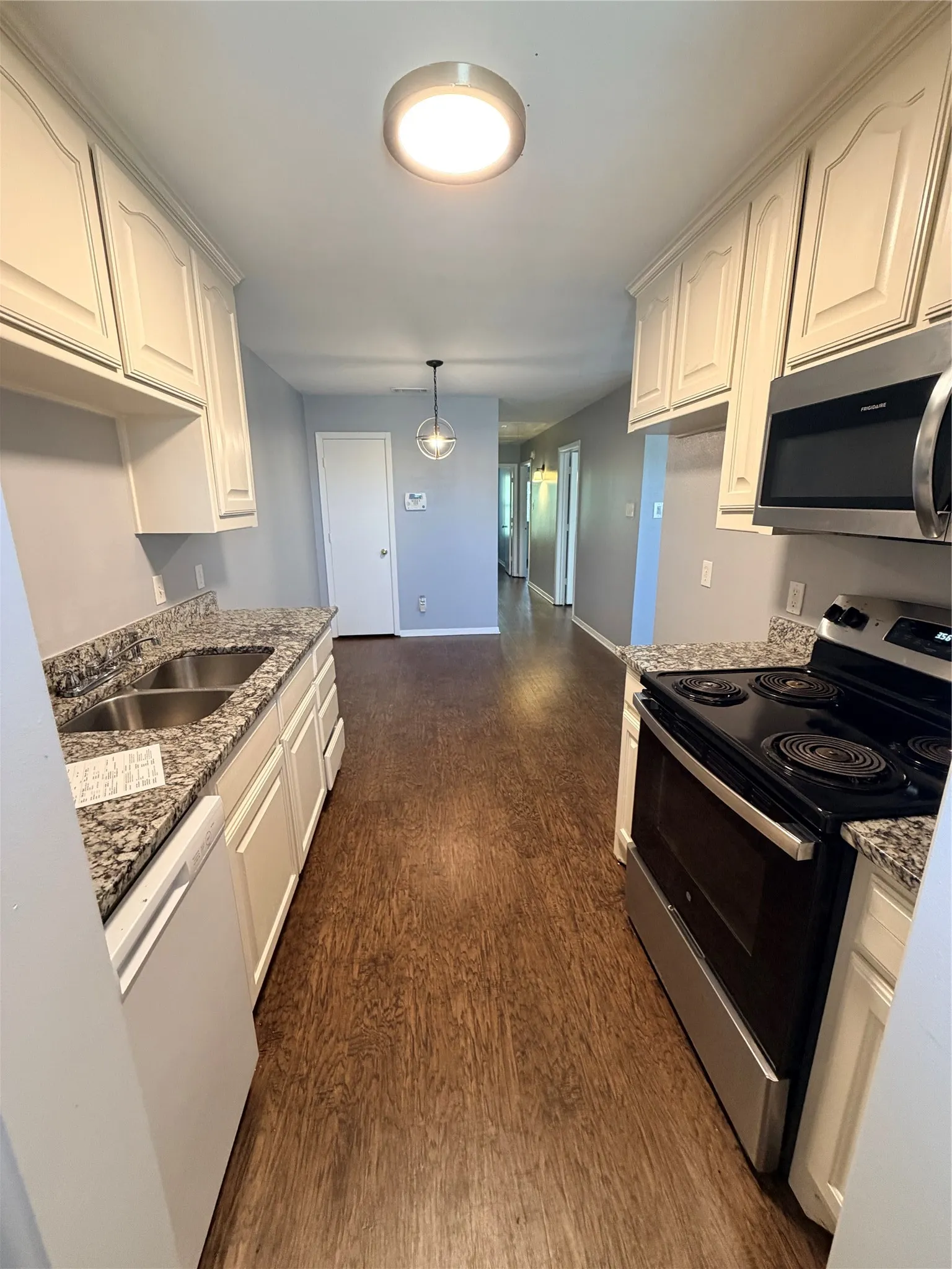 Galley kitchen featuring wood-finish flooring, white cabinetry, a double basin sink, and a built-in microwave