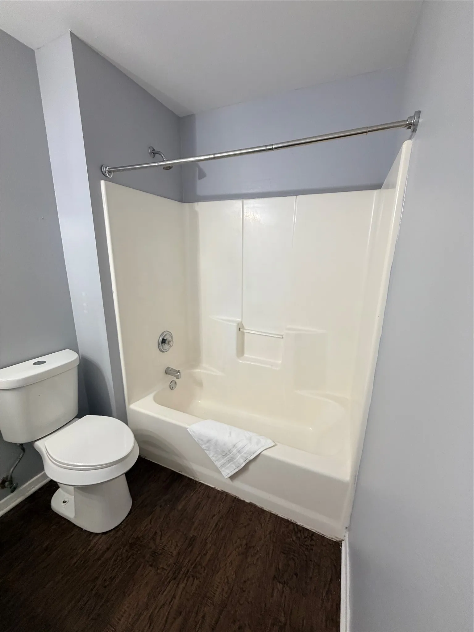 White toilet with a dark wood-finish floor and a white tub and shower combination