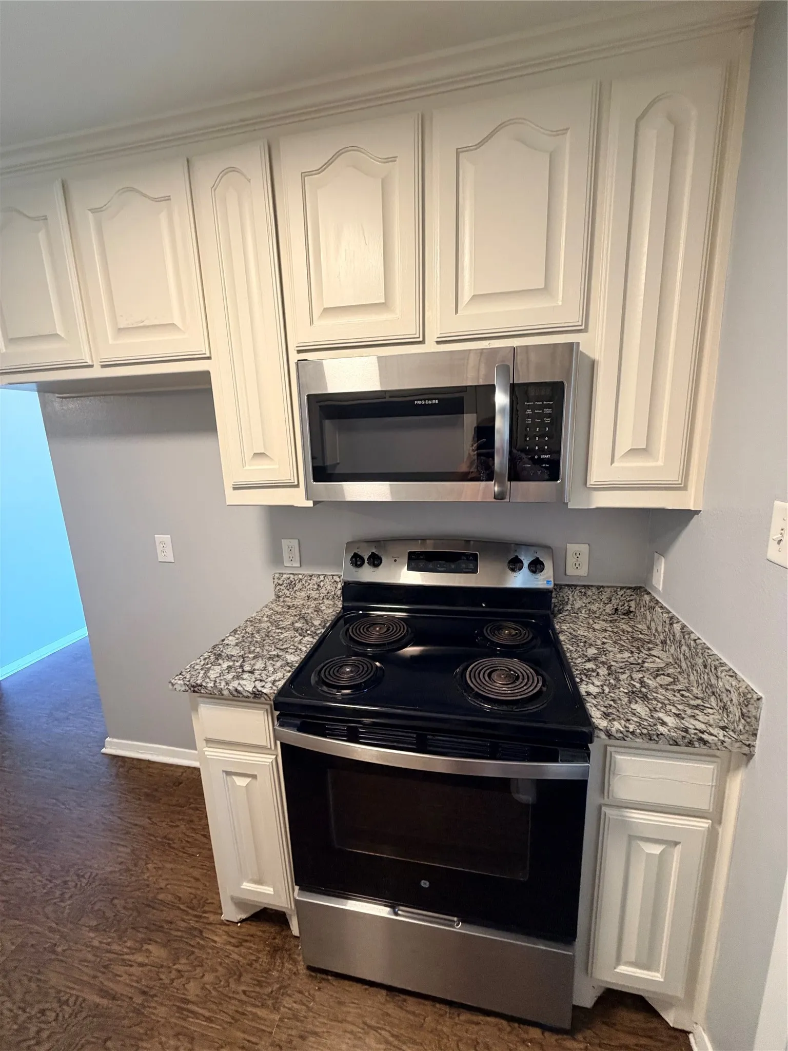 Kitchen featuring white cabinetry, stainless steel microwave, black electric range, and granite-style countertops