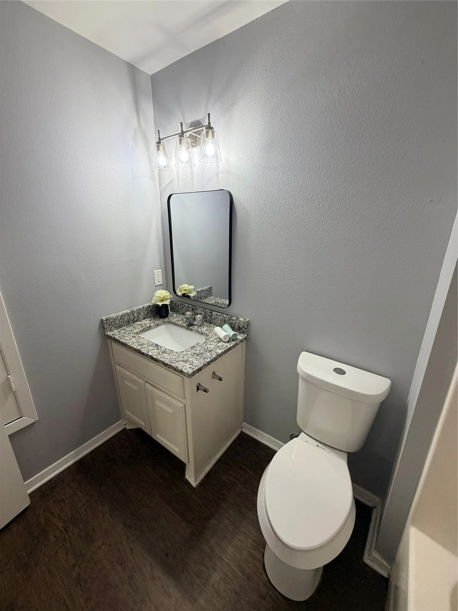 White vanity with a speckled countertop, undermount sink, and dark wood-finish flooring