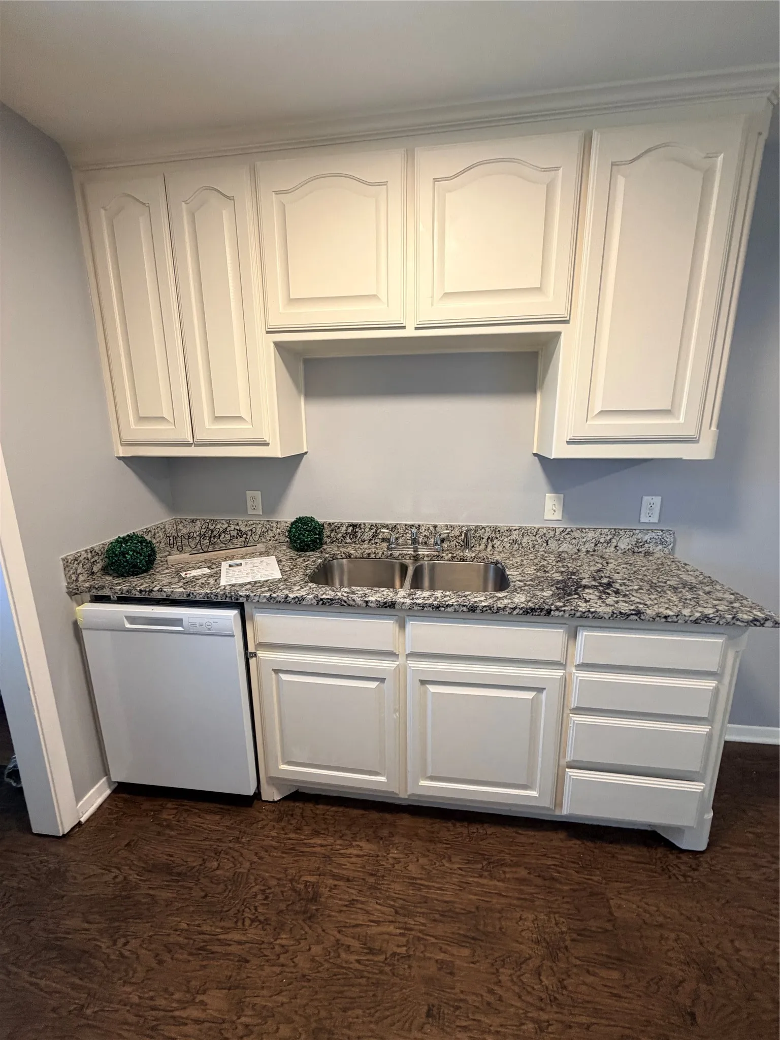 White cabinetry with crown molding, stainless steel double basin sink, granite-style countertops, and wood-finish flooring