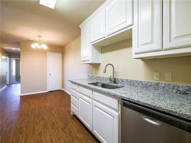 Kitchen featuring light stone counters, dishwasher, dark wood-type flooring, white cabinets, and a chandelier