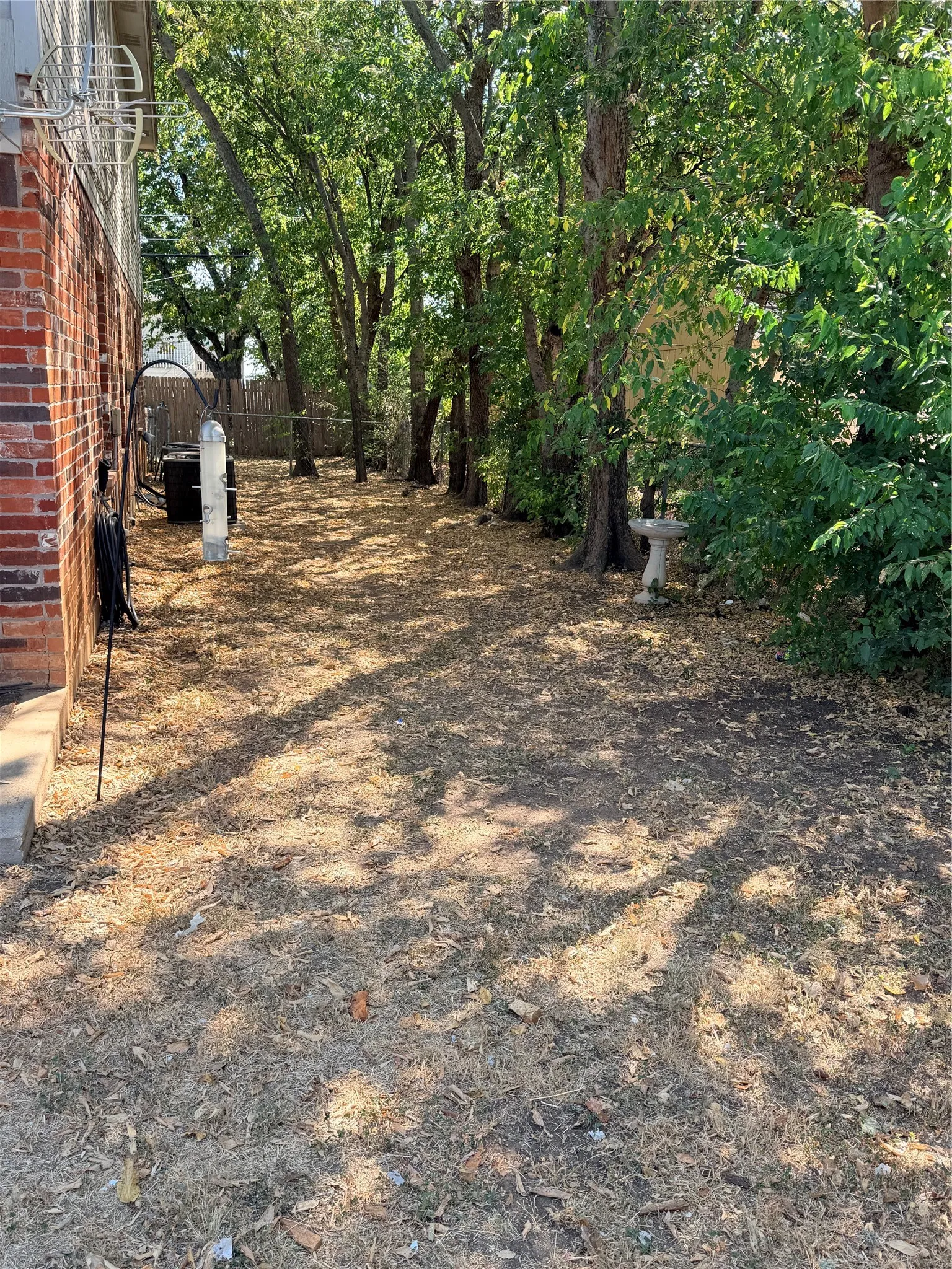 Brick exterior siding with a concrete foundation, mature trees, and natural ground cover