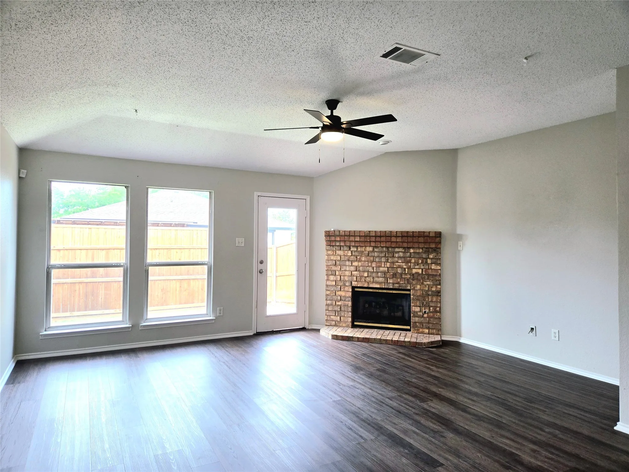 Vaulted ceiling, wood-finish flooring, brick fireplace, three pane windows, and a ceiling fan