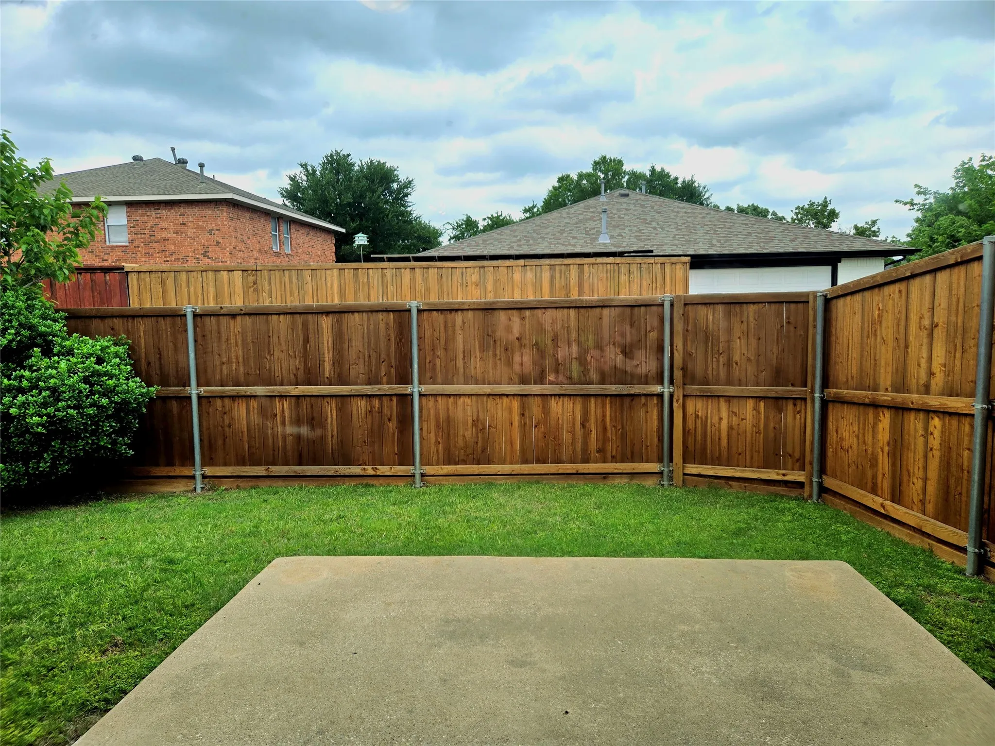 Concrete patio with a surrounding lawn, enclosed by a wood privacy fence