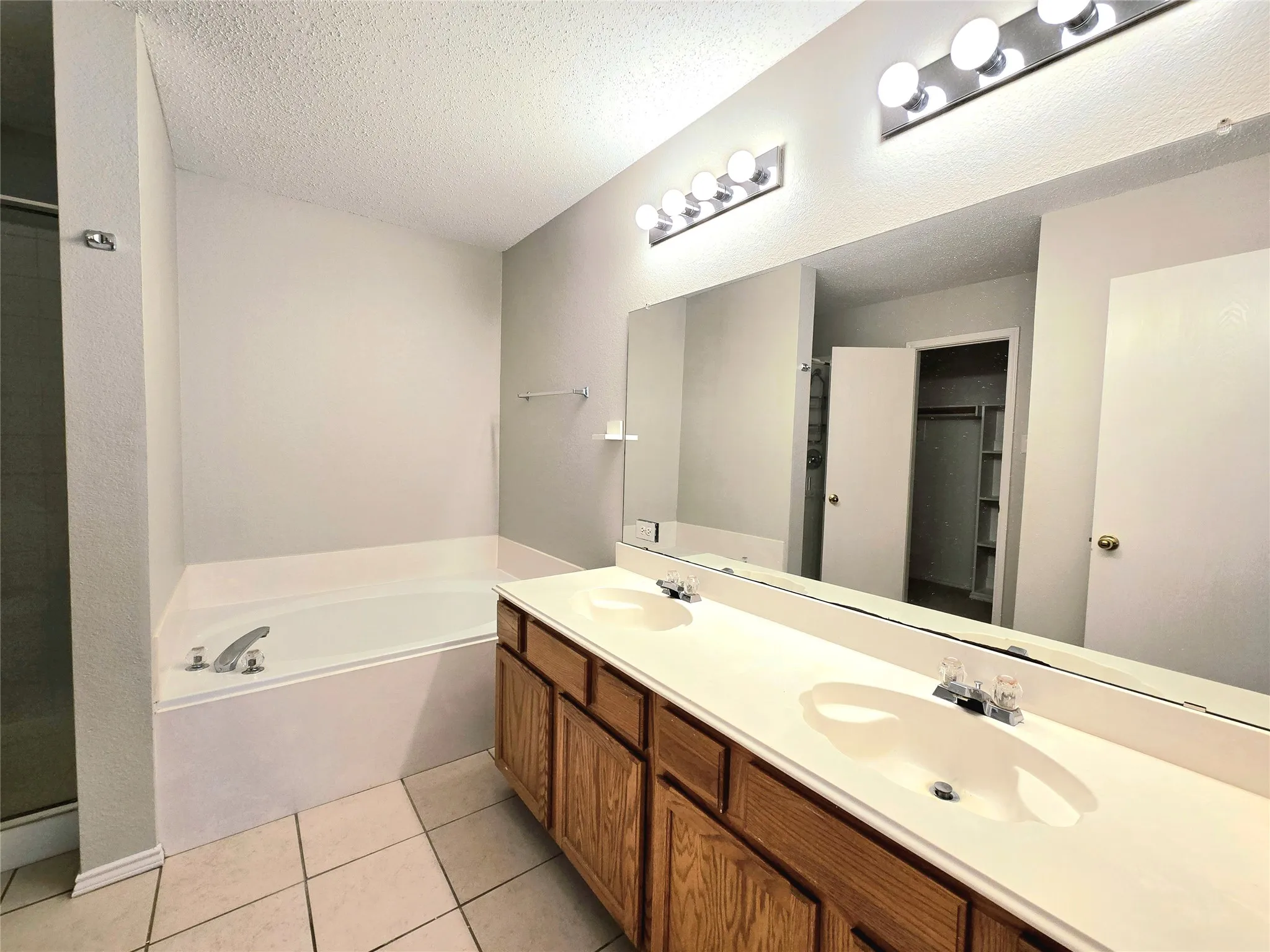Dual vanity with wood-finish cabinetry and integrated sinks, full-width mirror, and a built-in tub