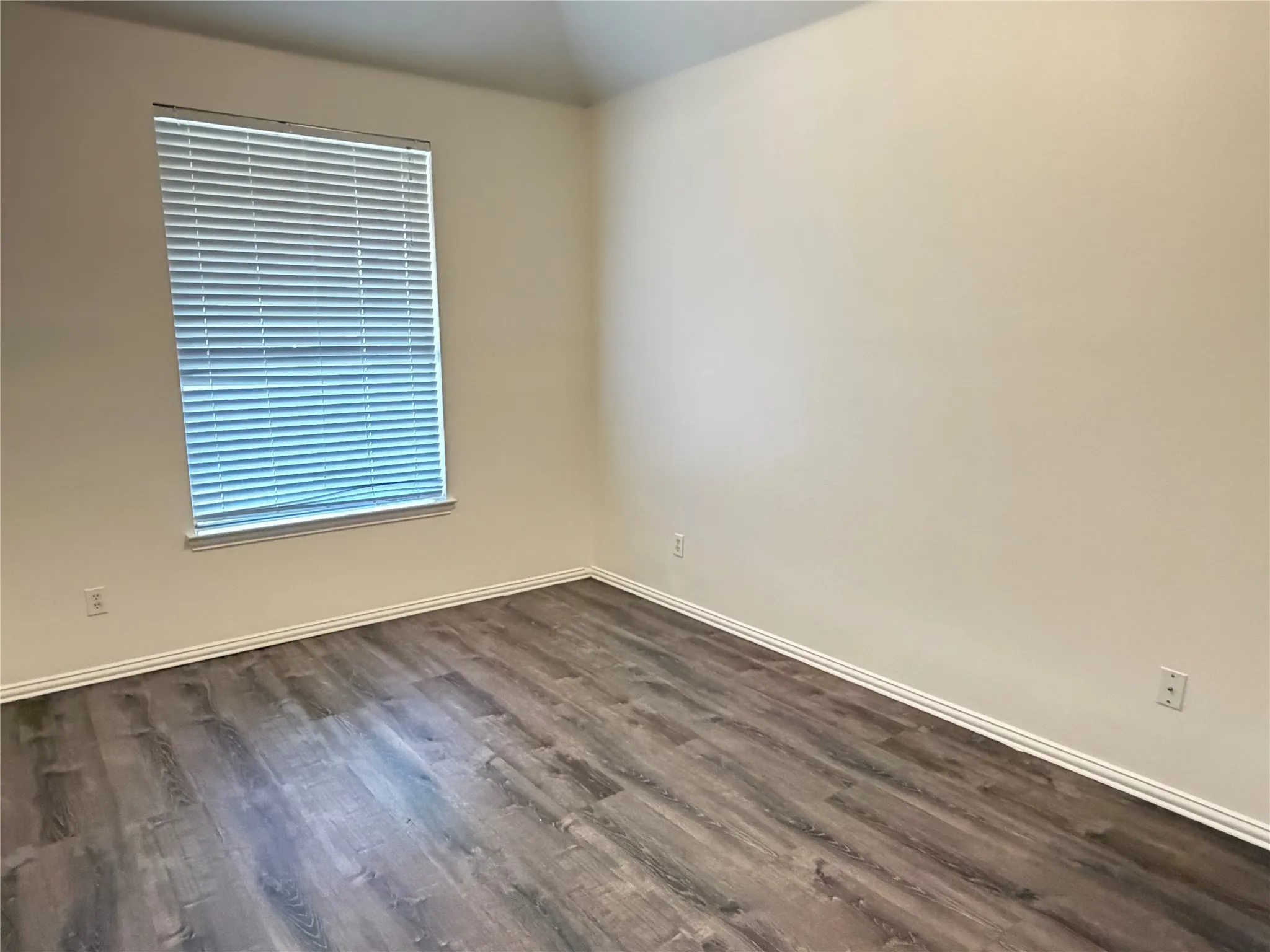 Room with wood-finish flooring, white baseboards, and neutral wall paint