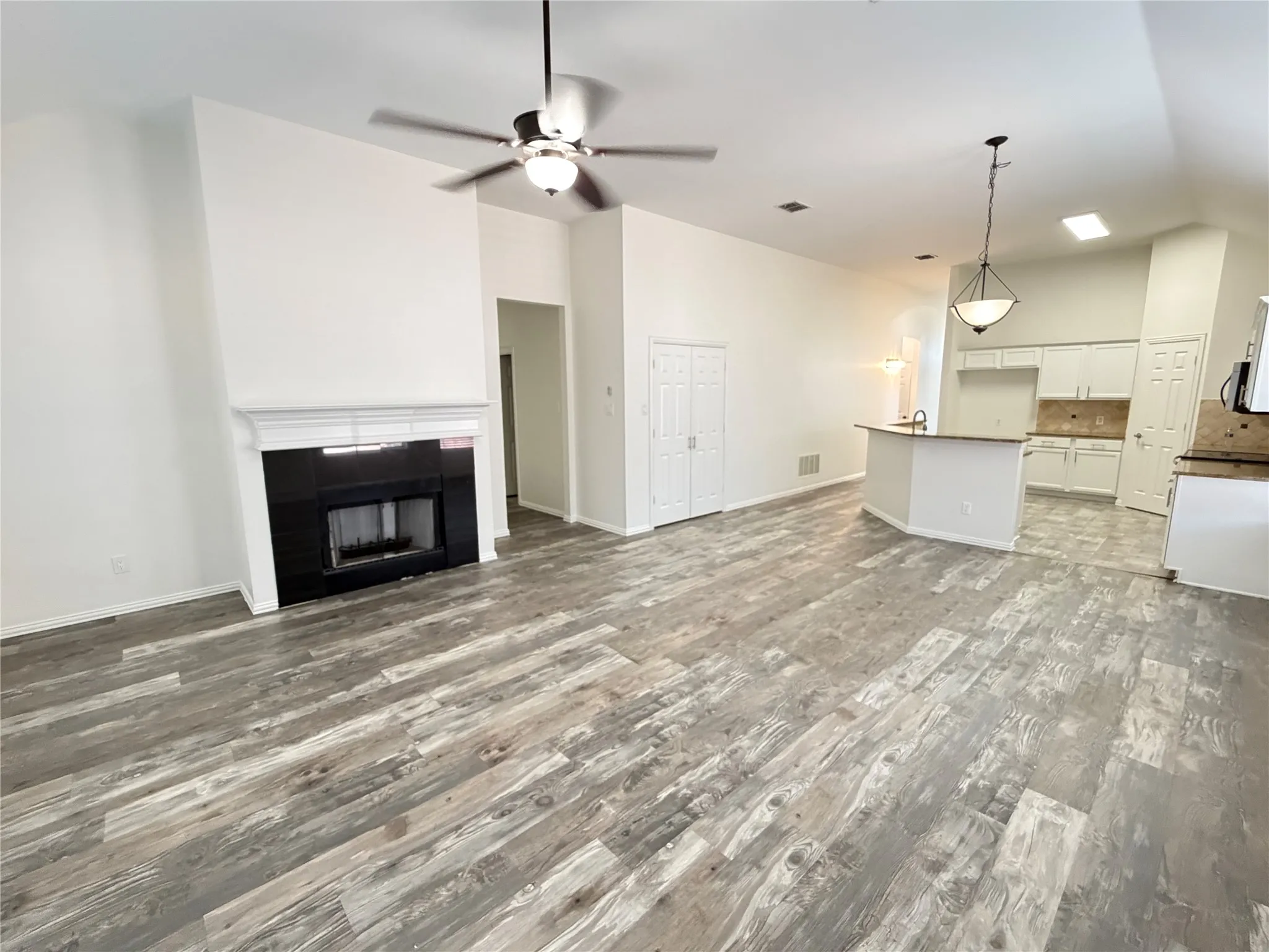 Open-concept living space featuring wood-finish flooring, a contemporary fireplace with a black surround and white mantel, and vaulted ceilings