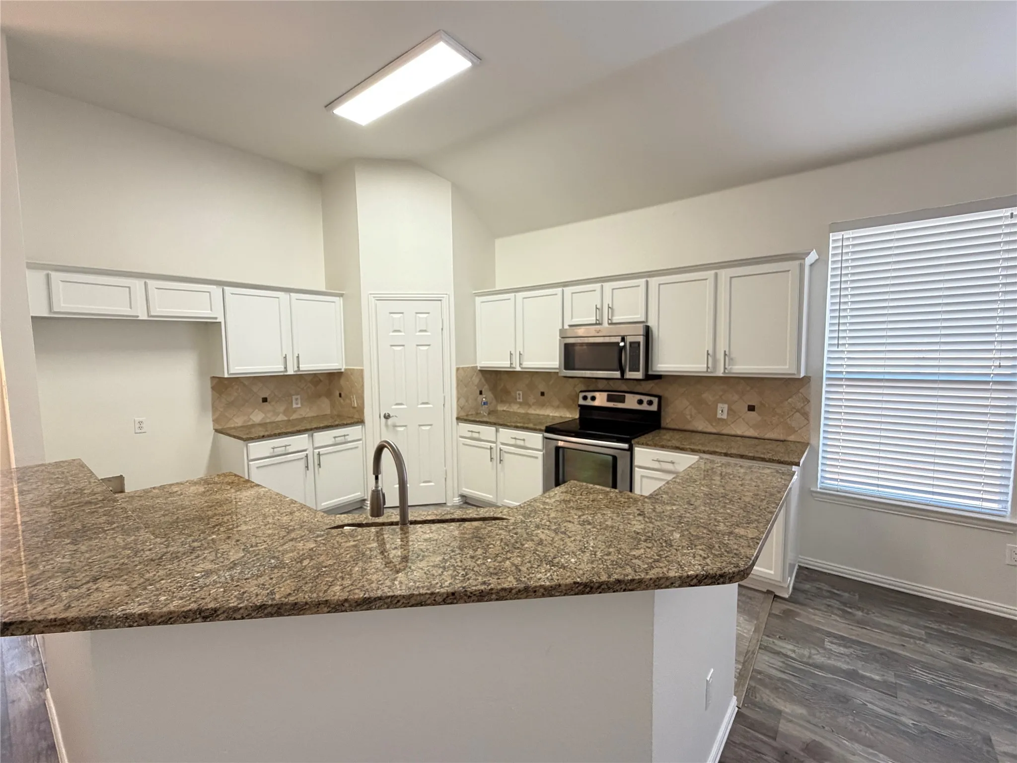 Modern kitchen featuring white cabinetry, stainless steel appliances, a tile backsplash, and granite countertops