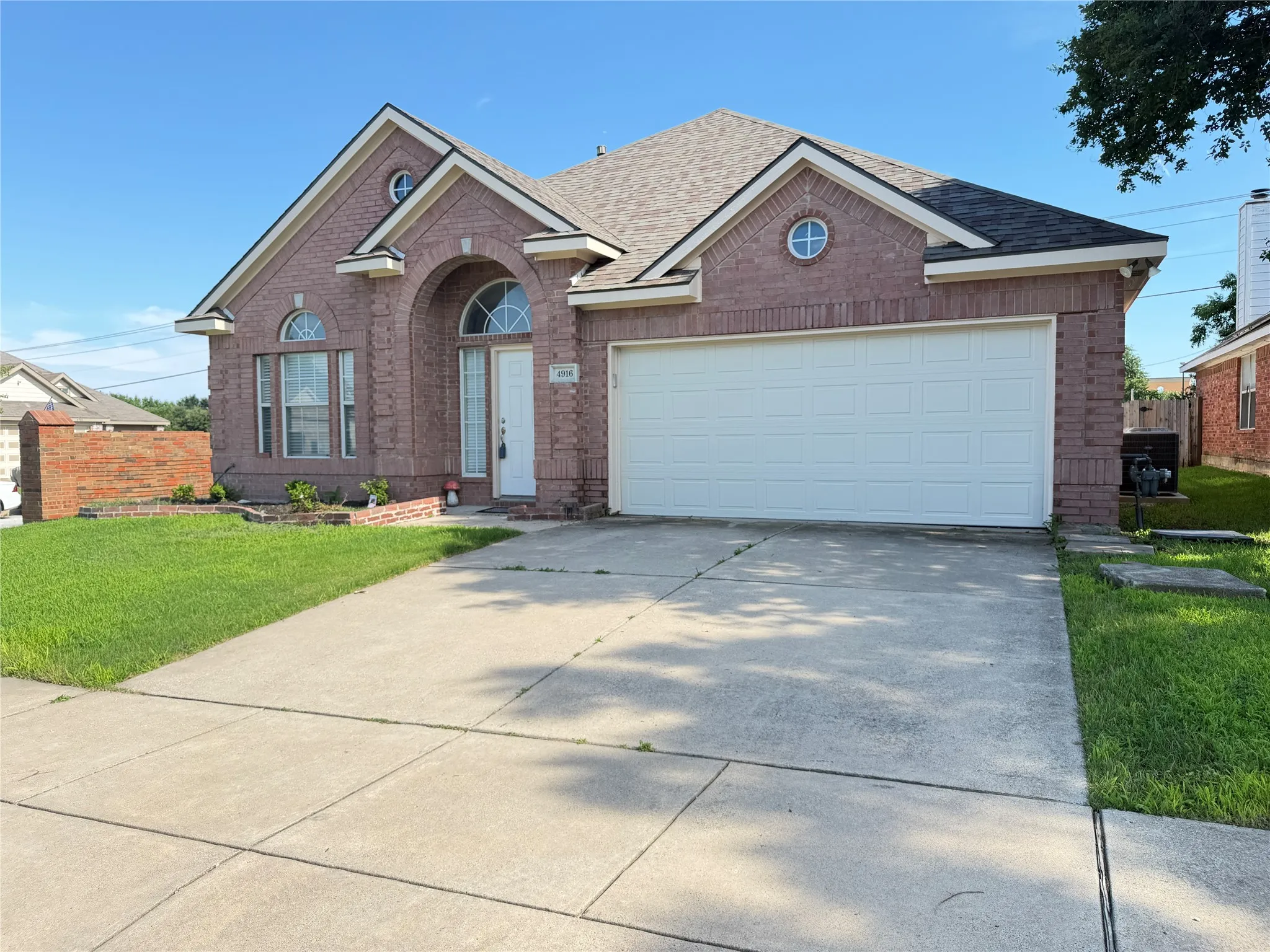 Brick exterior featuring an arched entryway, gabled roofline, and attached two-car garage