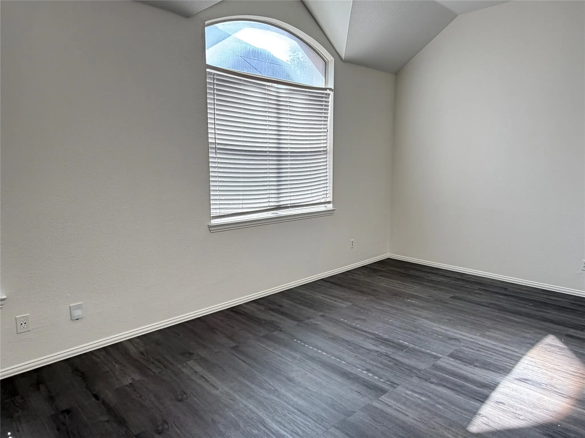 Room featuring a vaulted ceiling, an arched window with blinds, dark wood-finish flooring, and white baseboards