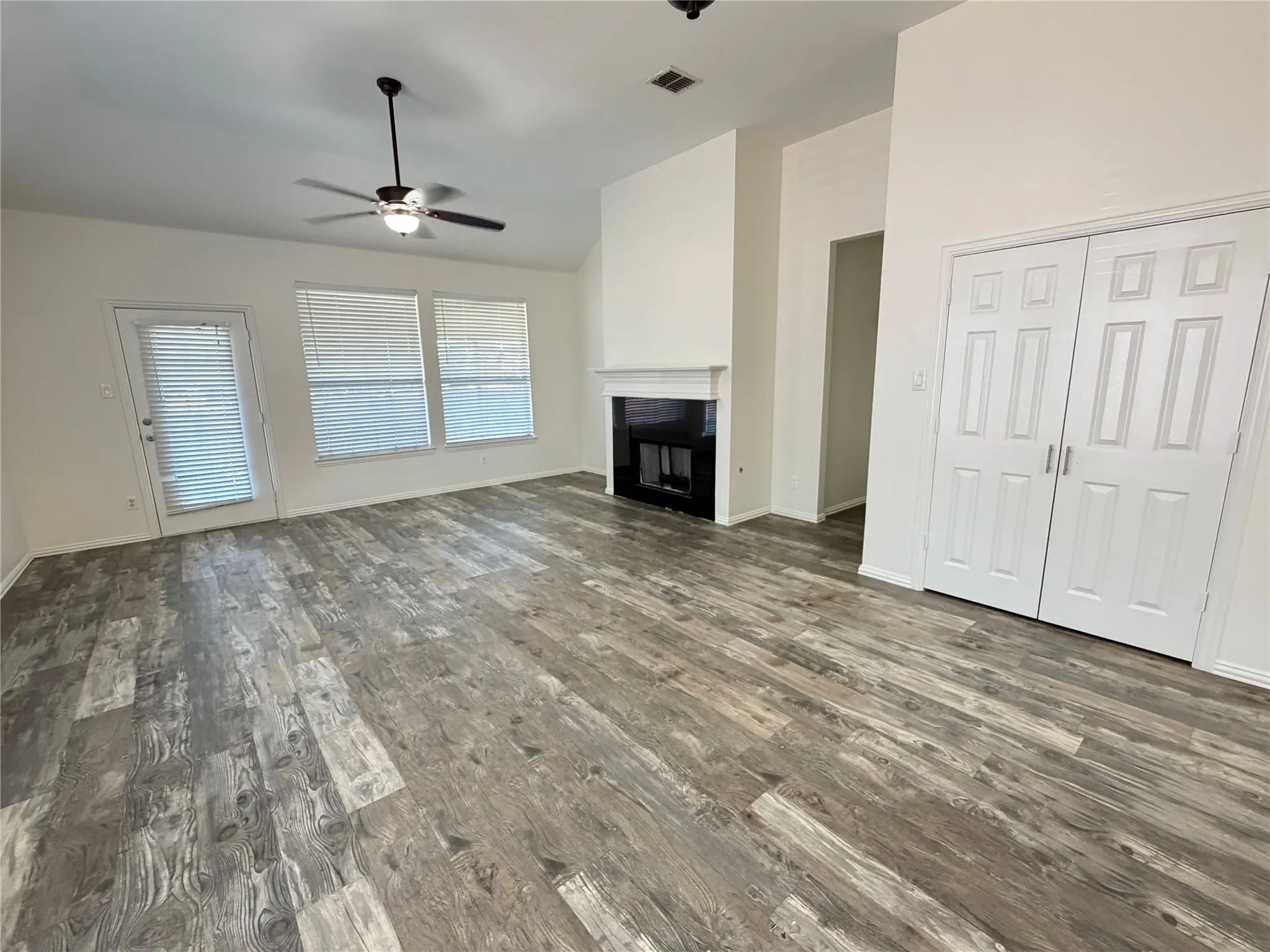 Spacious room featuring wood-finish flooring, a contemporary fireplace with a black insert, and vaulted ceilings