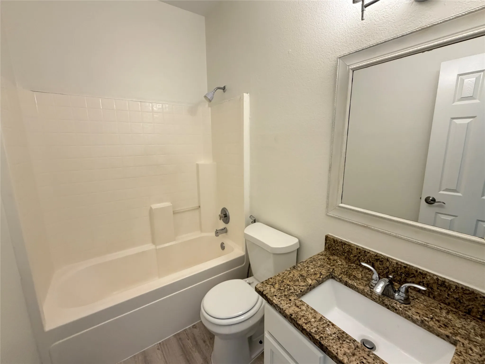 Bathroom featuring a combined tub and shower with tile surround, a vanity with a granite countertop and integrated sink, a large framed mirror, and wood-finish flooring