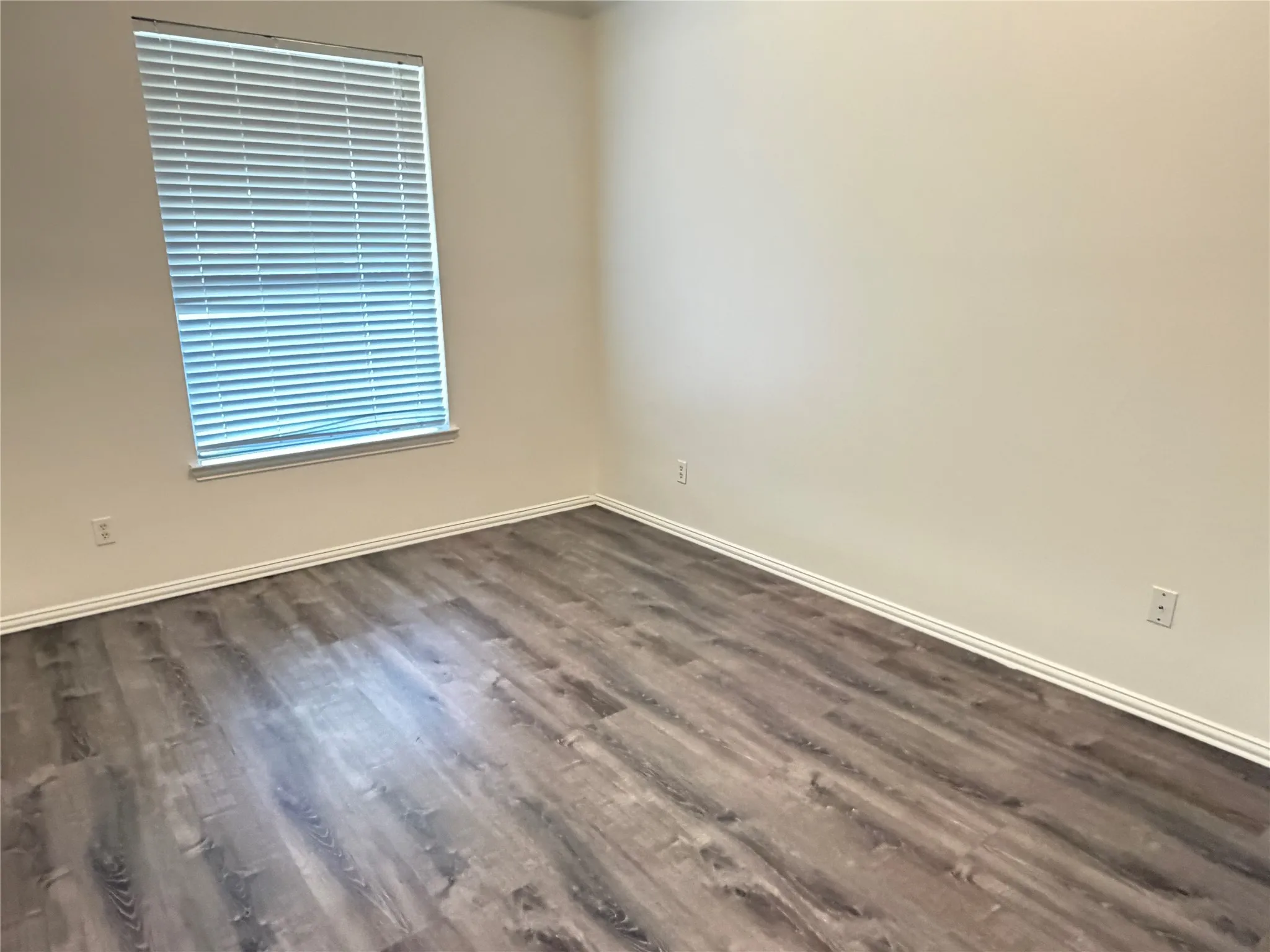 Interior room featuring wood-finish flooring, light-toned walls, and a window with horizontal blinds