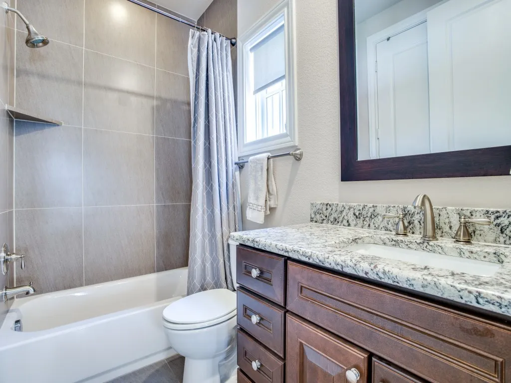 Bathtub with tiled surround, wood-finish vanity with a stone countertop, and an undermount sink