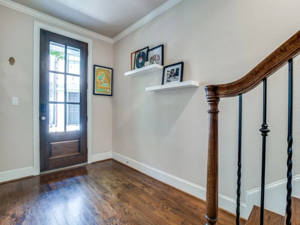 Hardwood flooring, wood-paneled door with glass inserts, detailed wooden handrail, wrought iron balusters, and crown molding