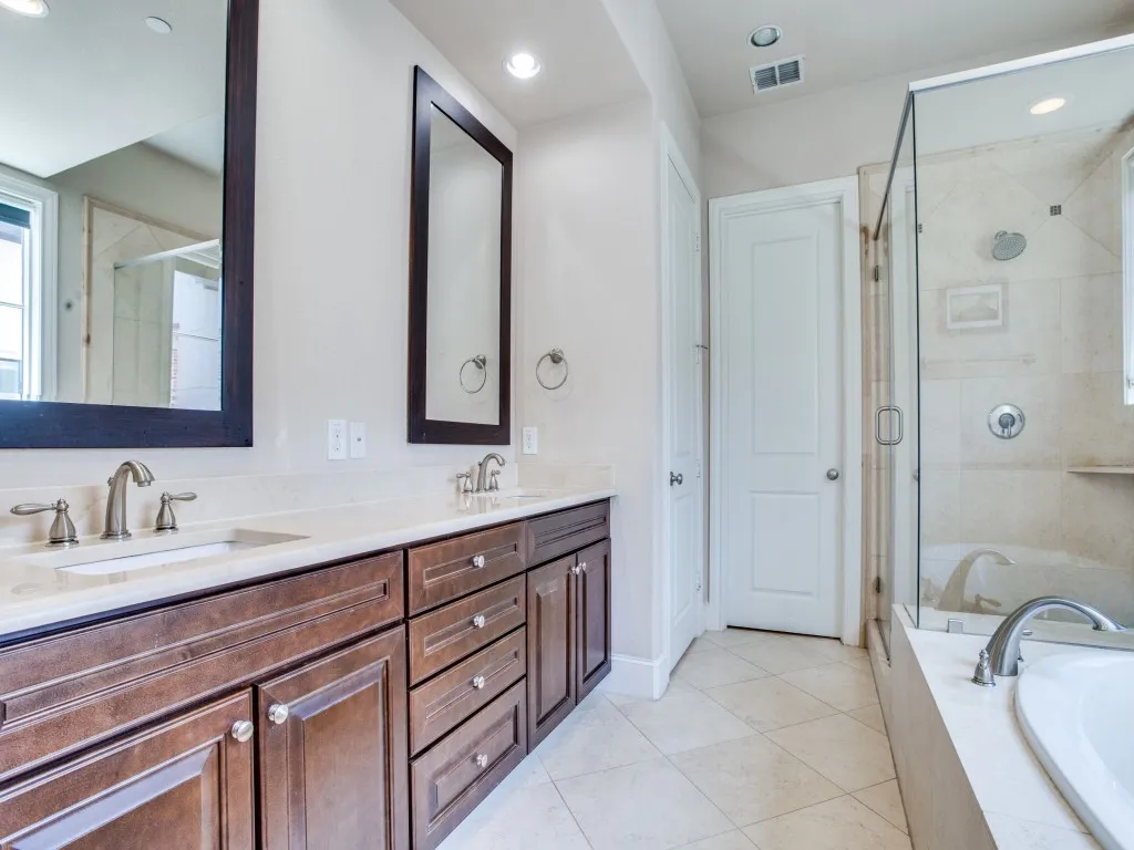 Dual vanity with undermount sinks and individual framed mirrors, solid surface countertops, extensive dark wood-finish cabinetry, tile flooring, and a glass-enclosed shower with a built-in bench