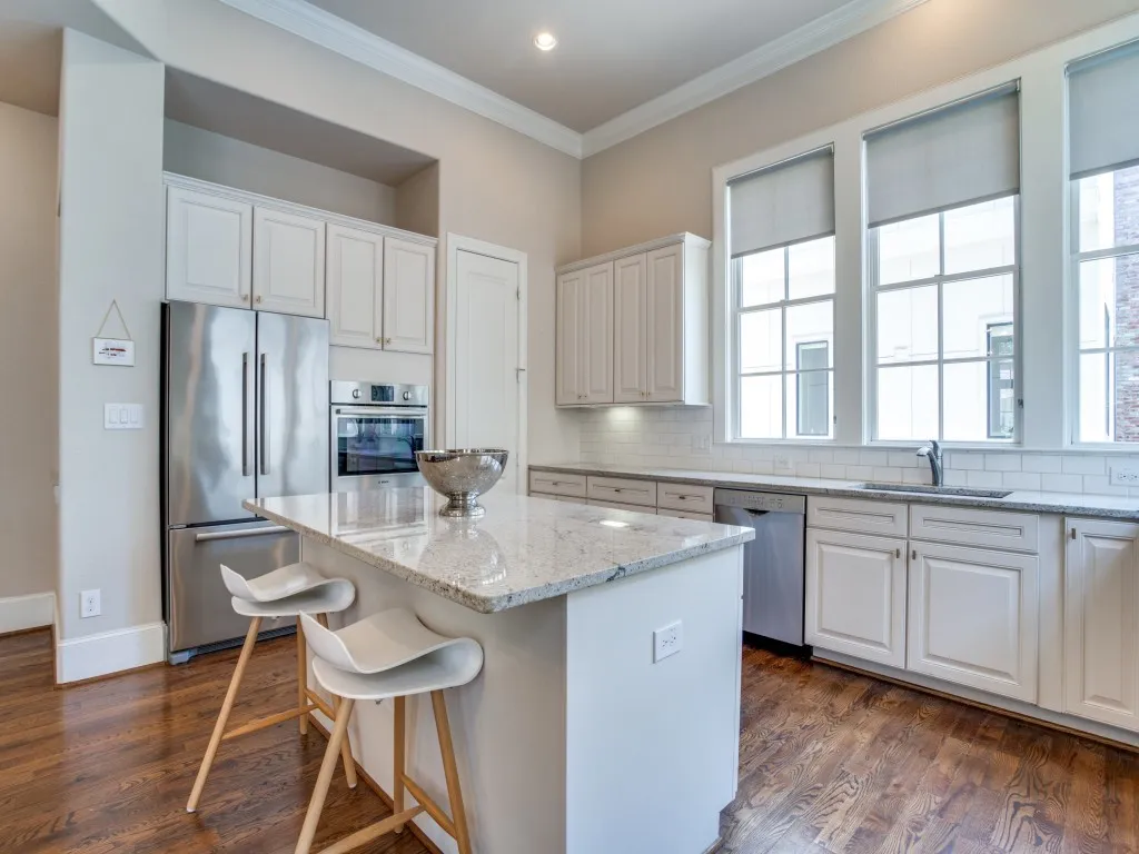 Kitchen featuring a large island with stone countertop, stainless steel appliances, abundant cabinetry, wood-finish flooring, and multiple large windows