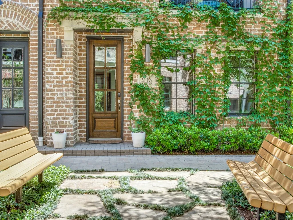 Brick exterior featuring climbing greenery, a wood-panelled glass door, and paver stone pathways