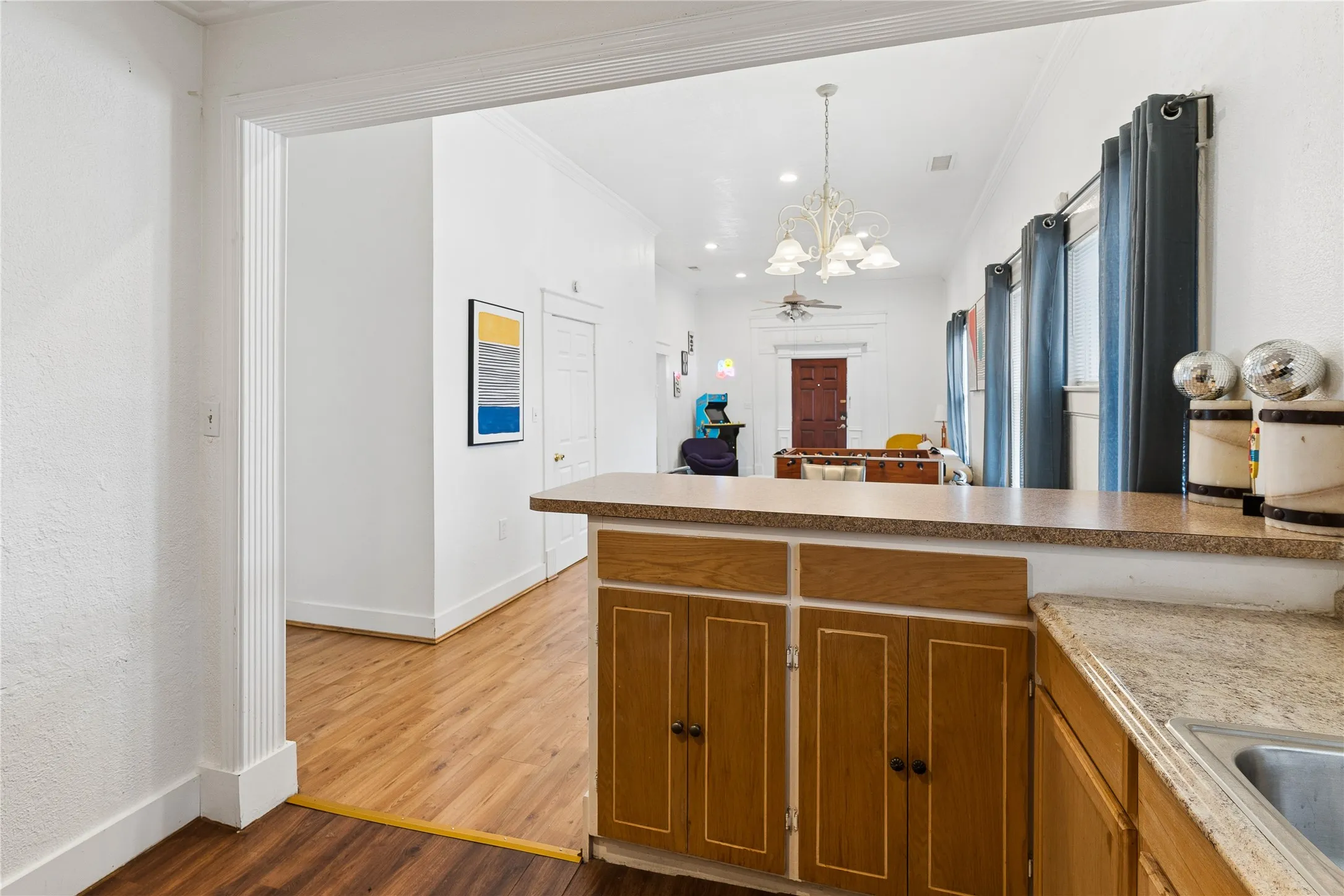 Wood-finish flooring throughout, light wood cabinetry with dark hardware, a built-in kitchen sink, and a durable countertop