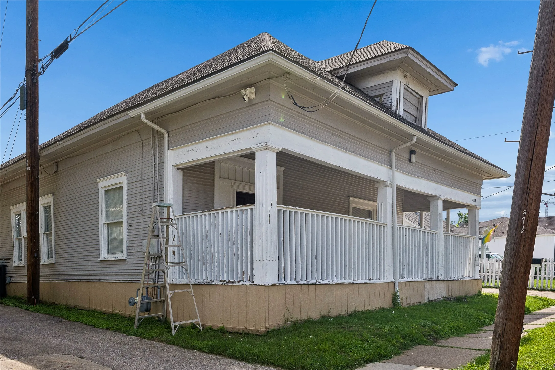 Exterior featuring a wraparound porch with white columns and railings, gray siding, and a gabled roof