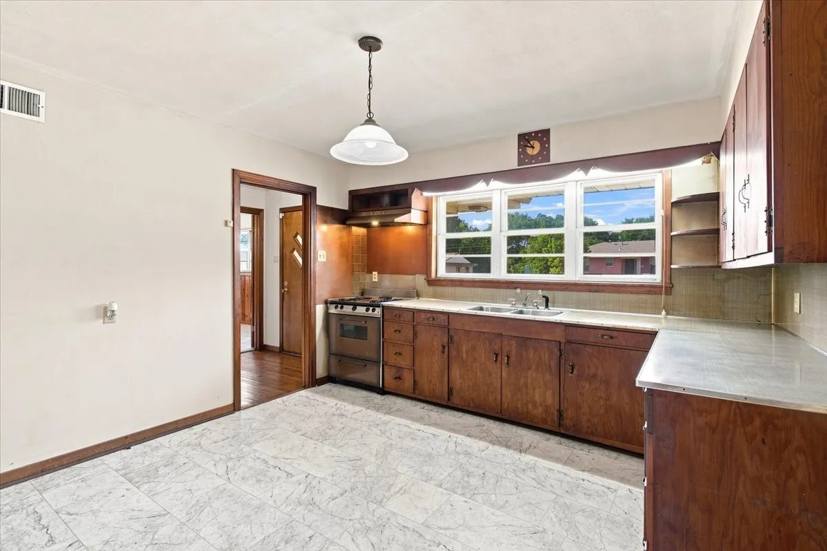 Kitchen featuring wood cabinetry, light-toned countertops, a gas range, a window above the sink, and freshly laid new flooring
