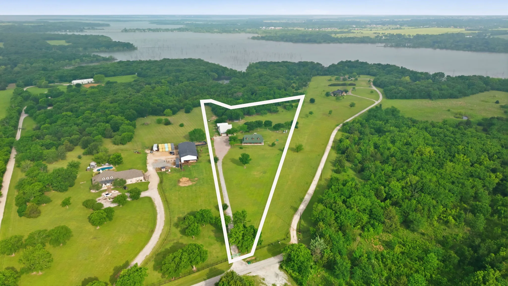 Expansive property featuring a residence, gravel driveway, and surrounding green landscape