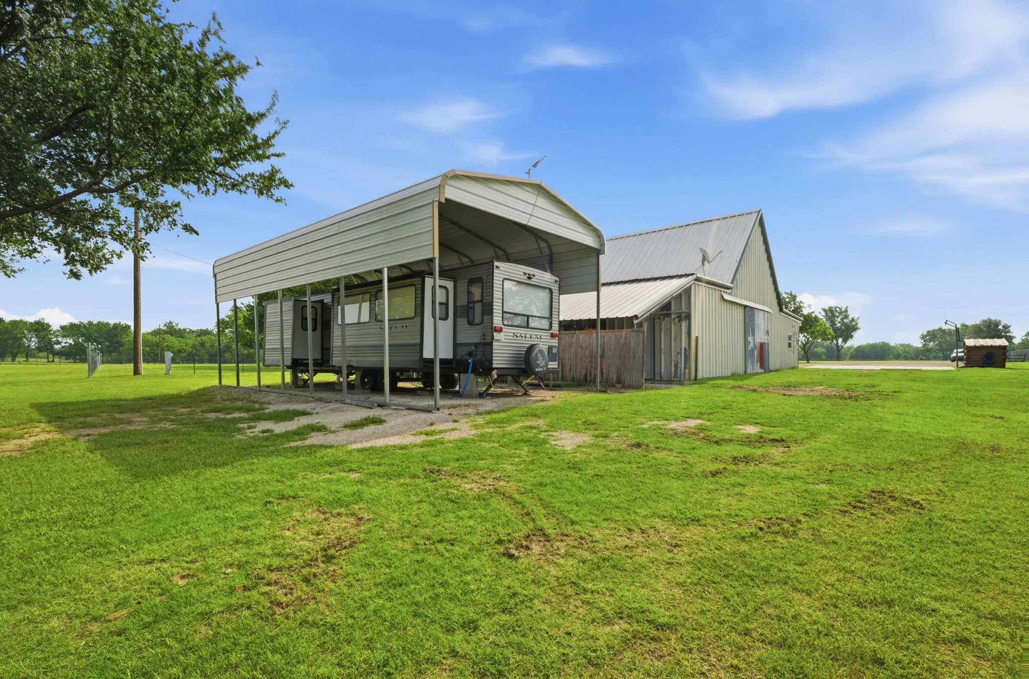 Expansive green space featuring a metal carport structure, a large barn with a metal roof, and a small outbuilding