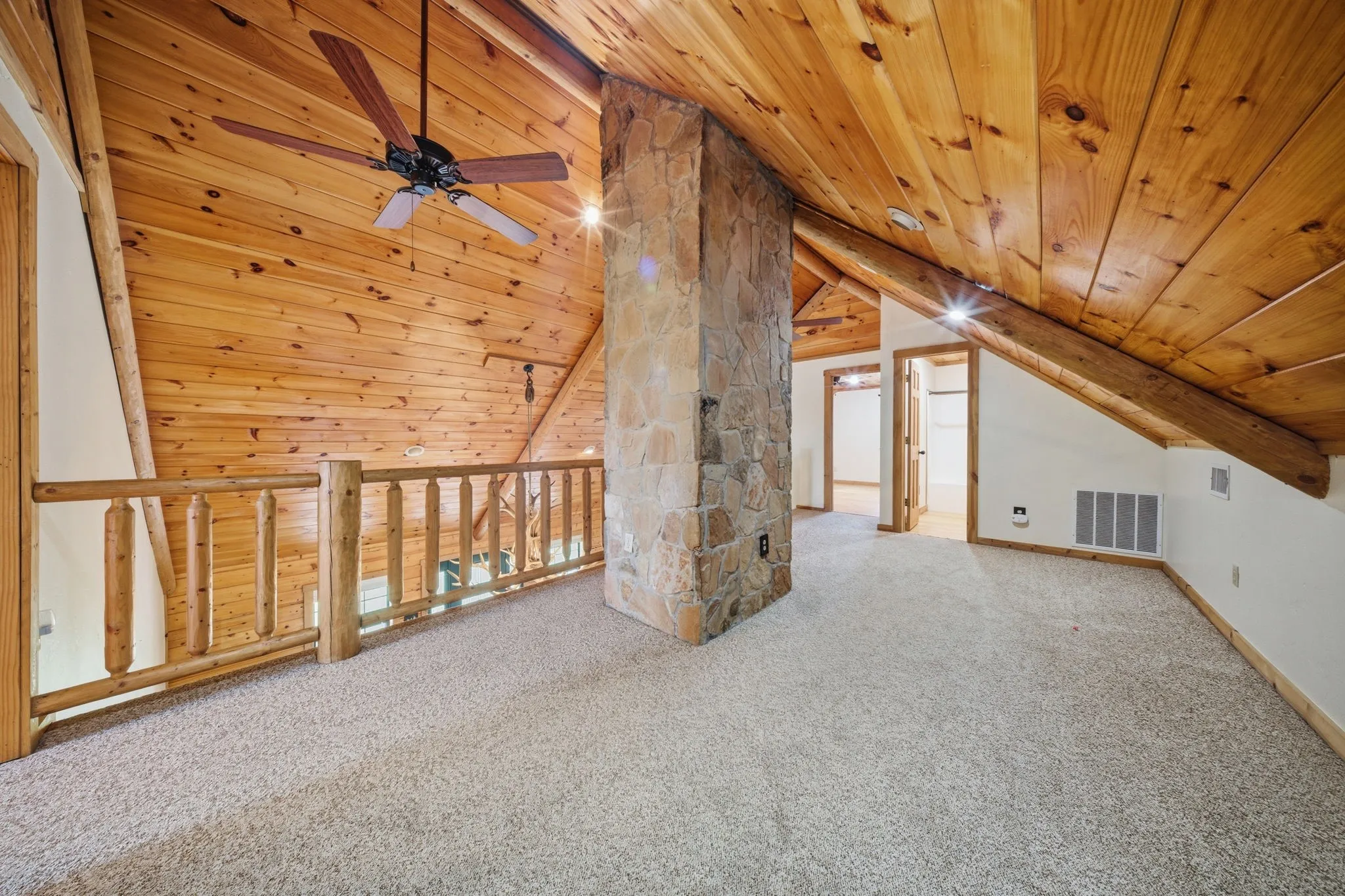 Loft area featuring sloped wood-paneled ceilings, wood railing, stone-clad pillar, and carpeted flooring