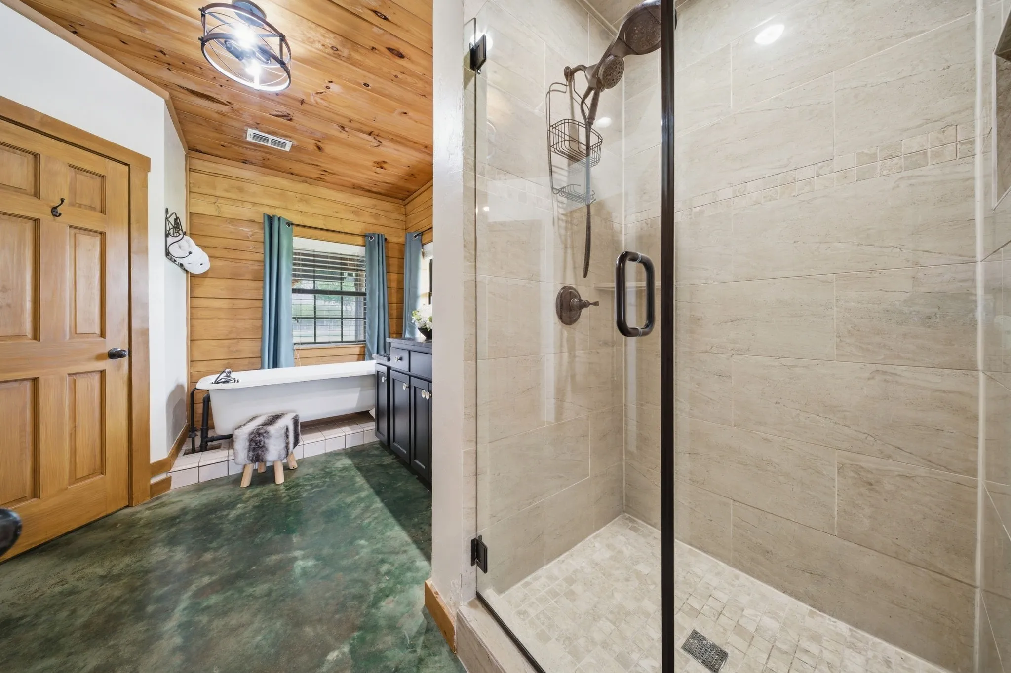 Glass-enclosed shower with tiled walls and floor, wood-paneled walls, wood-finish ceiling, and a freestanding bathtub
