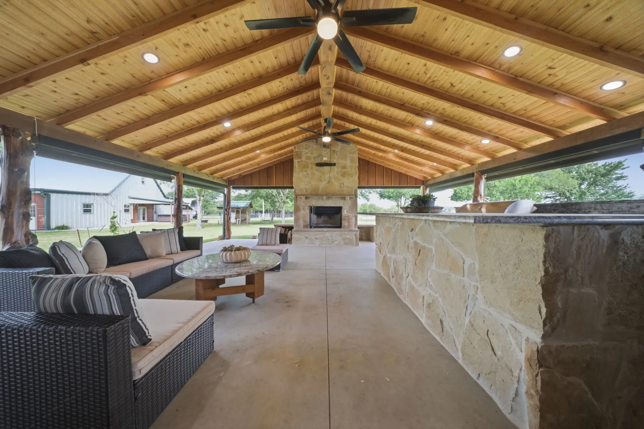Expansive covered outdoor living area featuring a vaulted wood-paneled ceiling, recessed lighting, and a stone-clad fireplace
