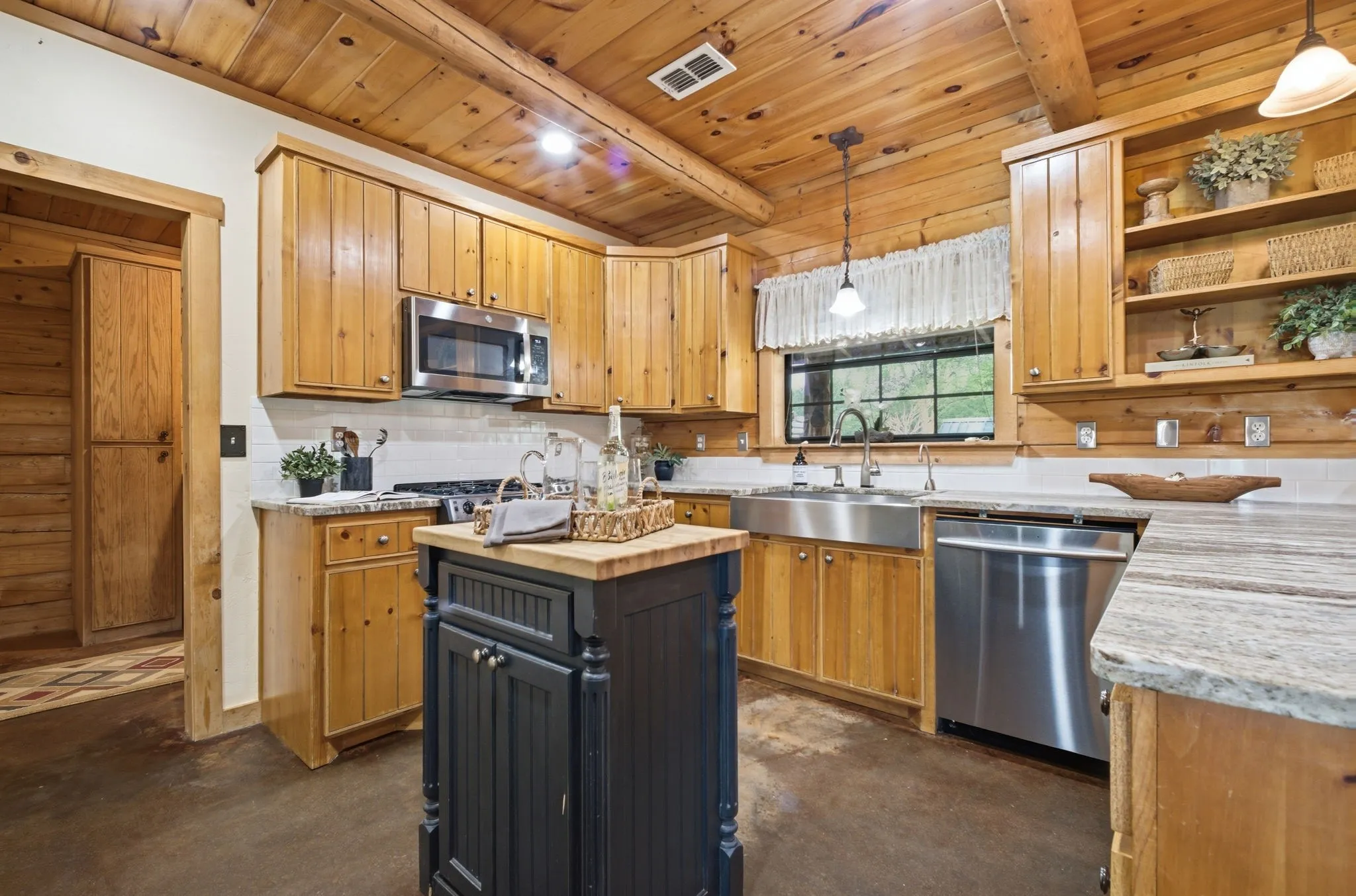Wood-paneled ceilings, wood cabinetry, stone countertops, stainless steel appliances, and a farmhouse-style sink