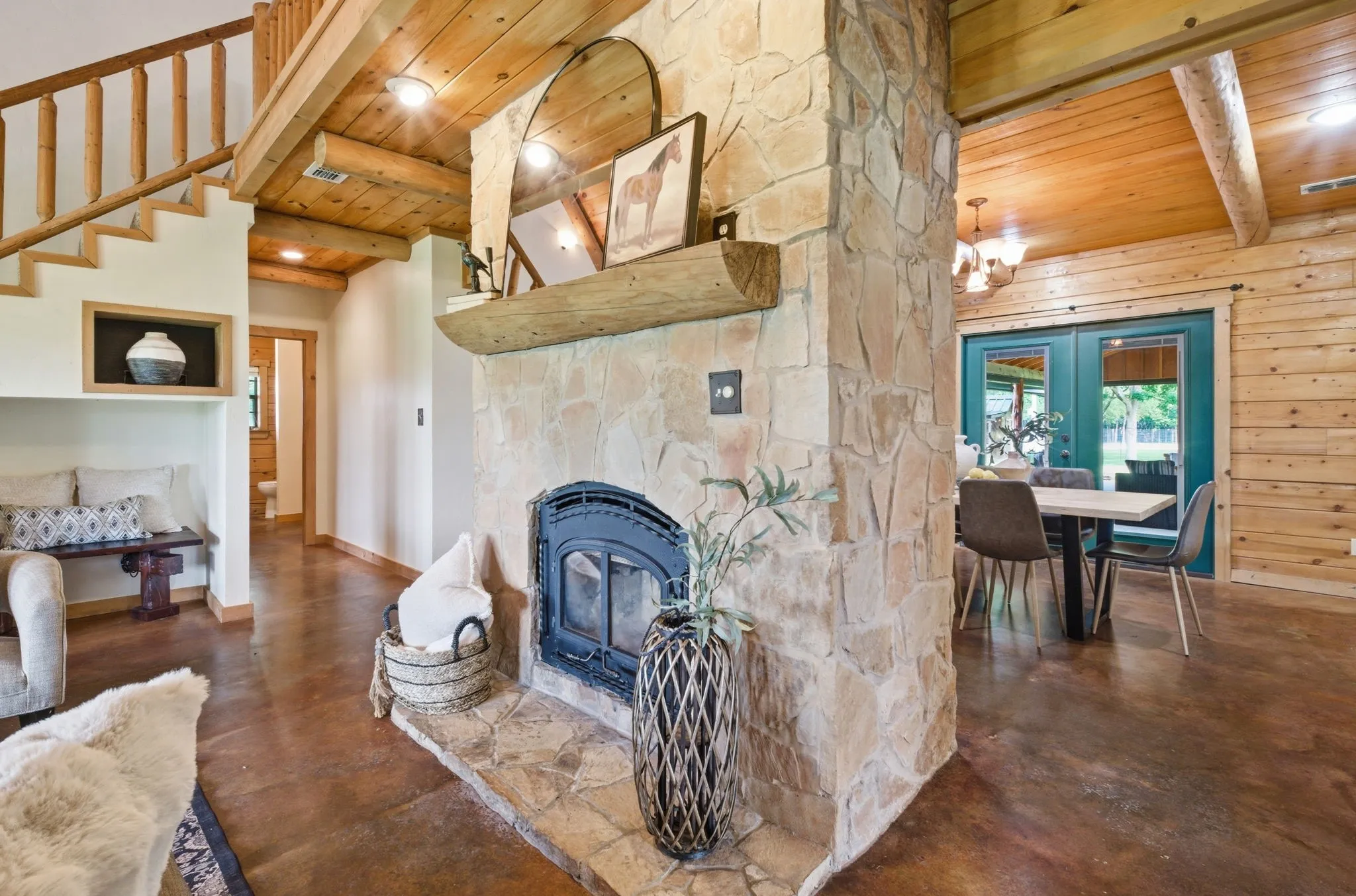 Stone fireplace with hearth, wood-finish flooring, natural wood ceiling, wood beam accents, and a wood staircase with a log railing