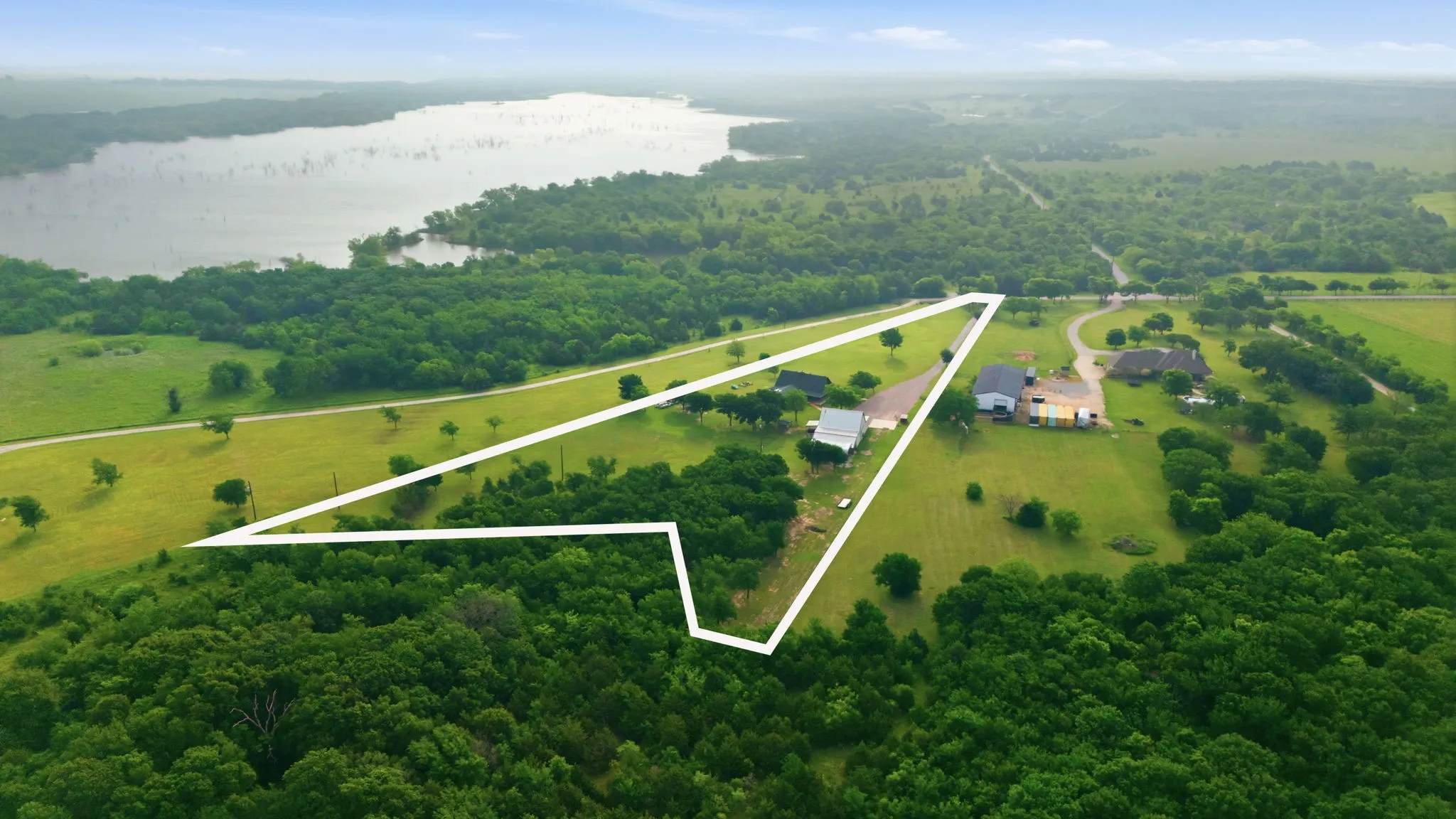 Expansive property featuring a large lake, mature trees, open grassy areas, and a paved road