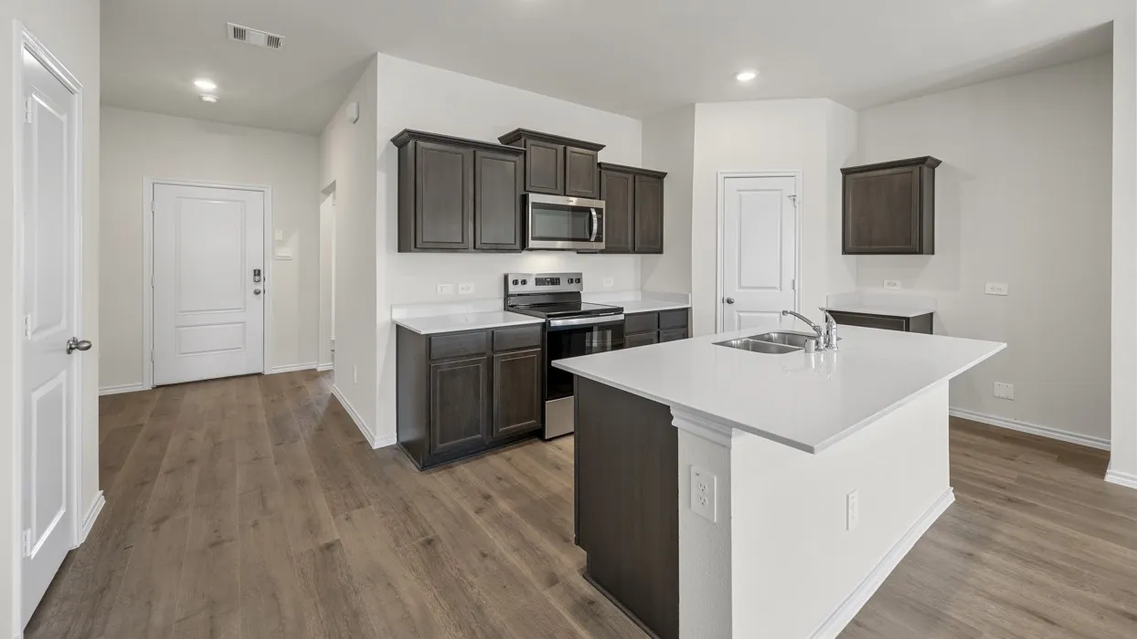 Modern kitchen featuring dark wood-finish cabinetry, stainless steel appliances, a center island with sink, white countertops, and wood-finish flooring