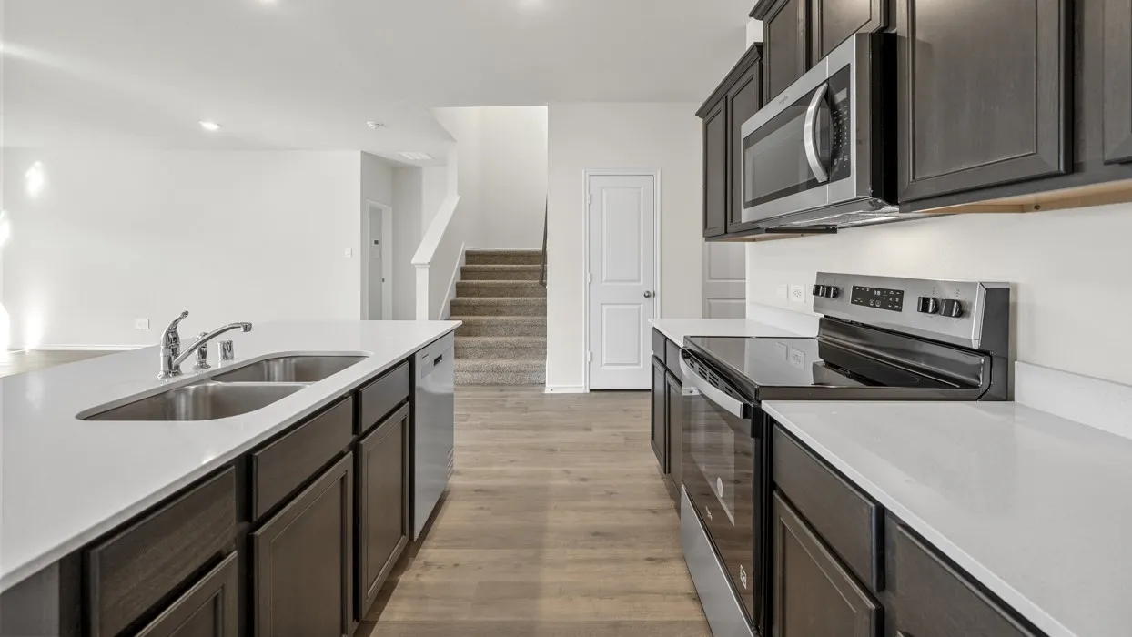 Kitchen featuring dark wood-finish cabinetry, light-toned countertops, stainless steel appliances, and a double basin sink with a chrome faucet