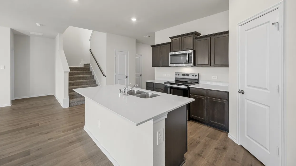 Modern kitchen with dark wood-finish cabinetry, stainless steel appliances, and a central island featuring a stainless steel double sink