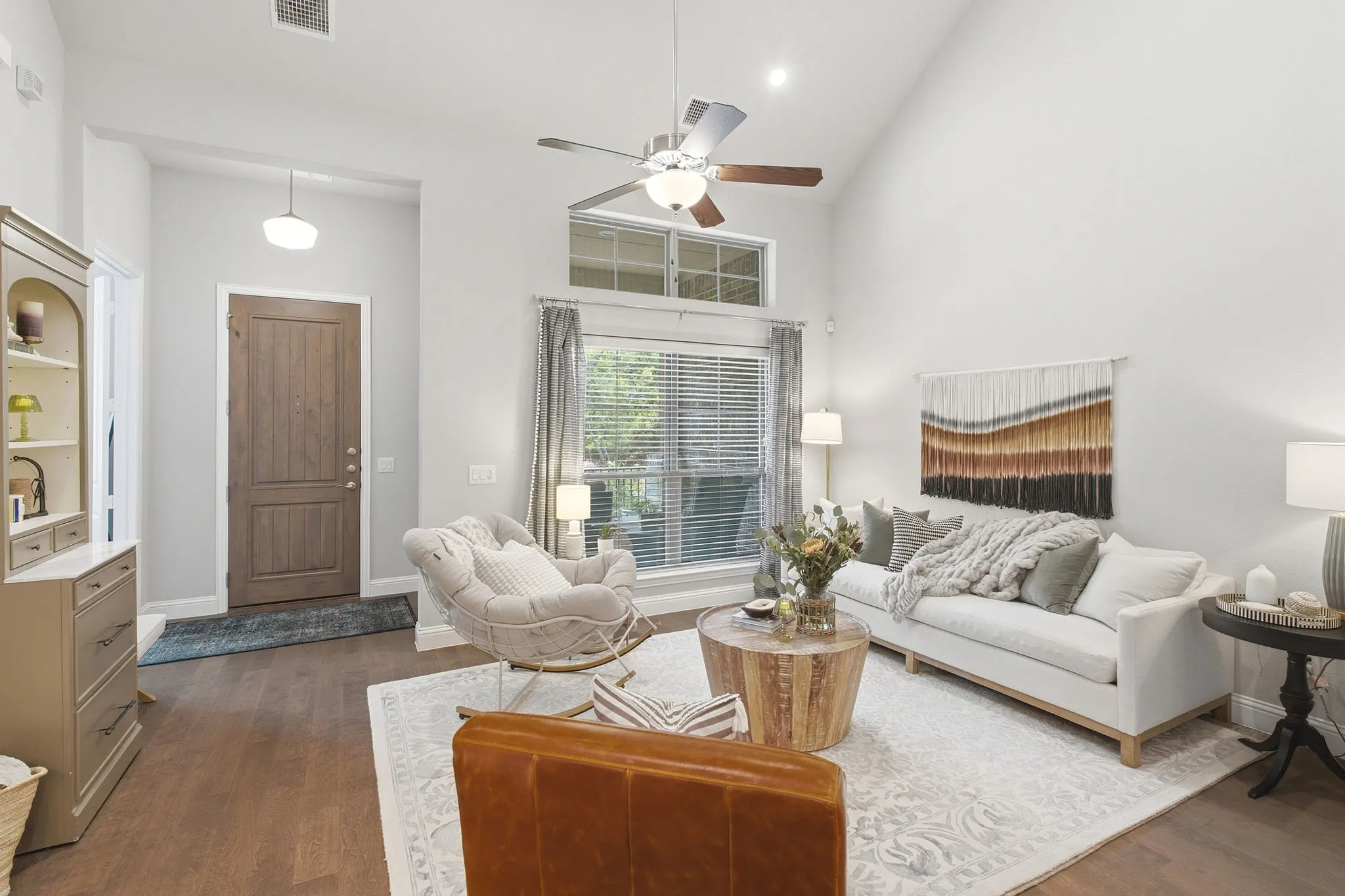 Living area with soaring ceilings, wood-finish flooring, a ceiling fan, and large windows with blinds