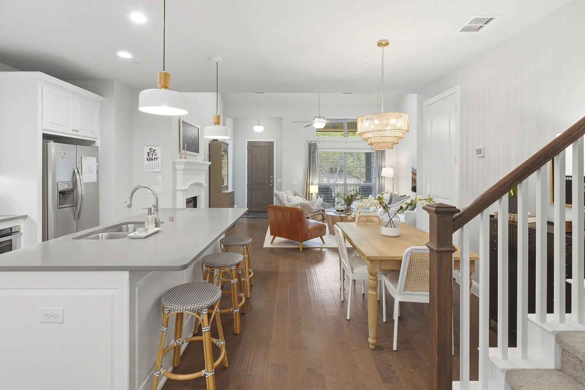 Open-concept living space featuring wood-finish flooring, a kitchen island with integrated sink, stainless steel appliances, and a staircase with white risers and wood handrail