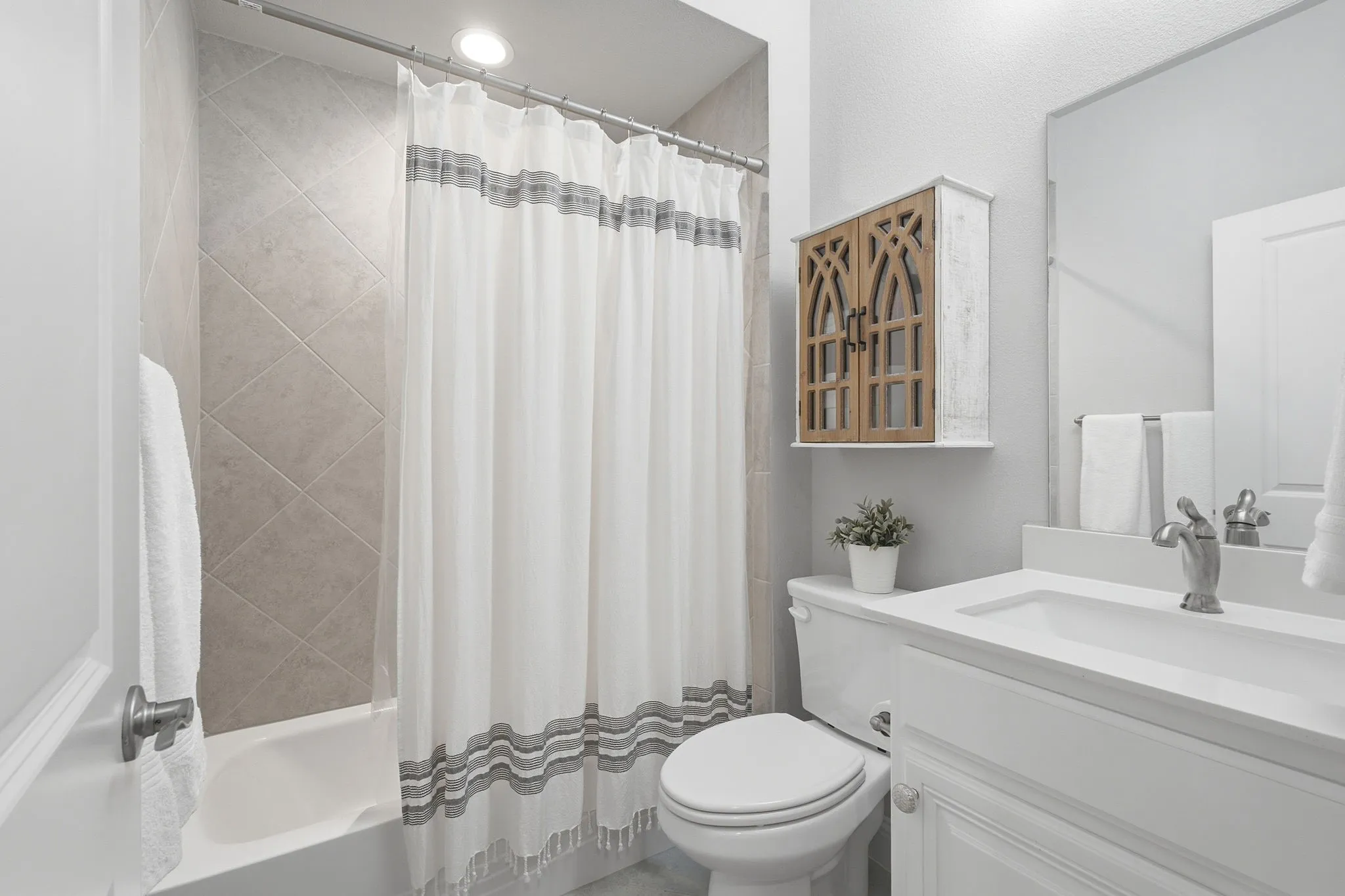 Bathtub with tiled surround, white vanity with integrated sink, chrome faucet, and wall-mounted​​‌​​​​‌​​‌‌​‌‌​​​‌‌​‌​‌​‌​​​‌​​ mirror