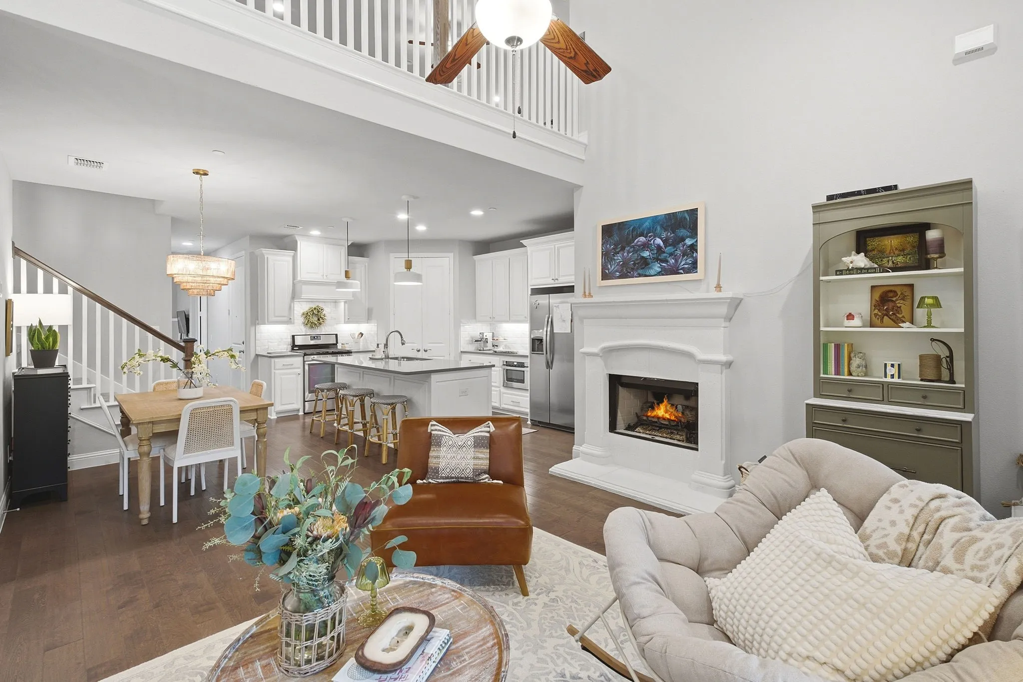 Open-concept living area with wood-finish flooring, a white fireplace, and a high ceiling