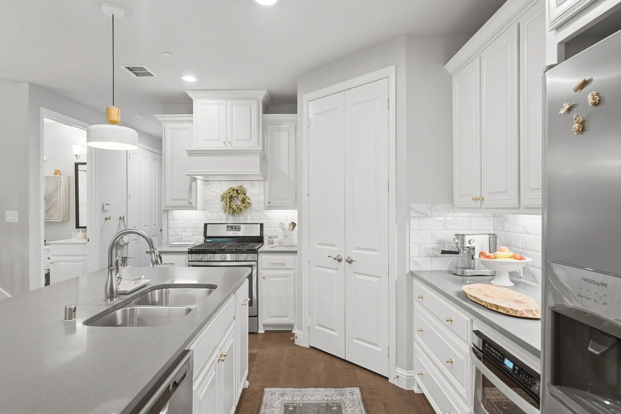 White shaker cabinetry, stainless steel appliances, wood-finish flooring, undermount double-basin sink, and a large central island with a solid surface countertop