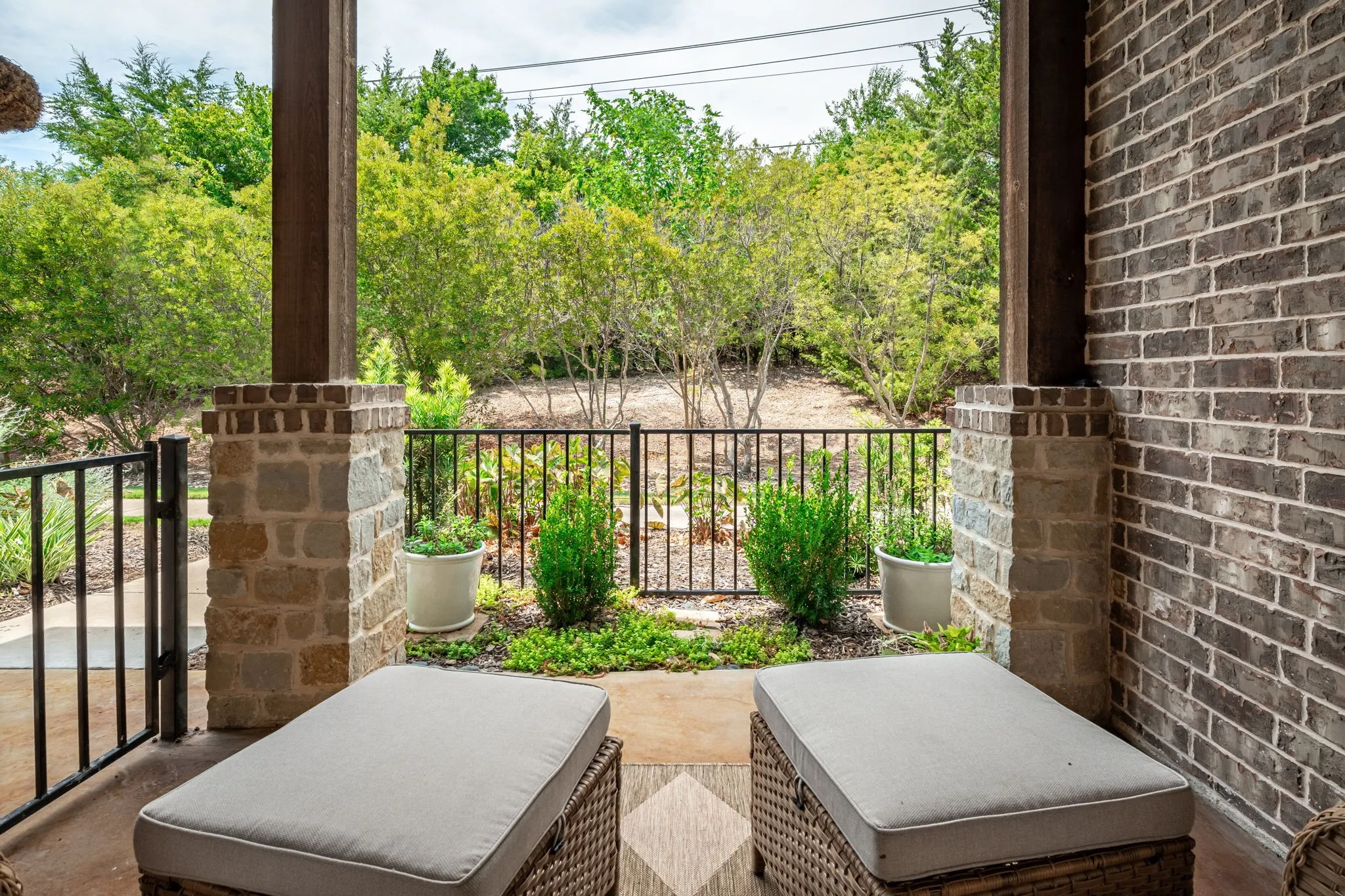 Covered patio featuring a brick and stone pillar, dark brick exterior wall, and metal railing