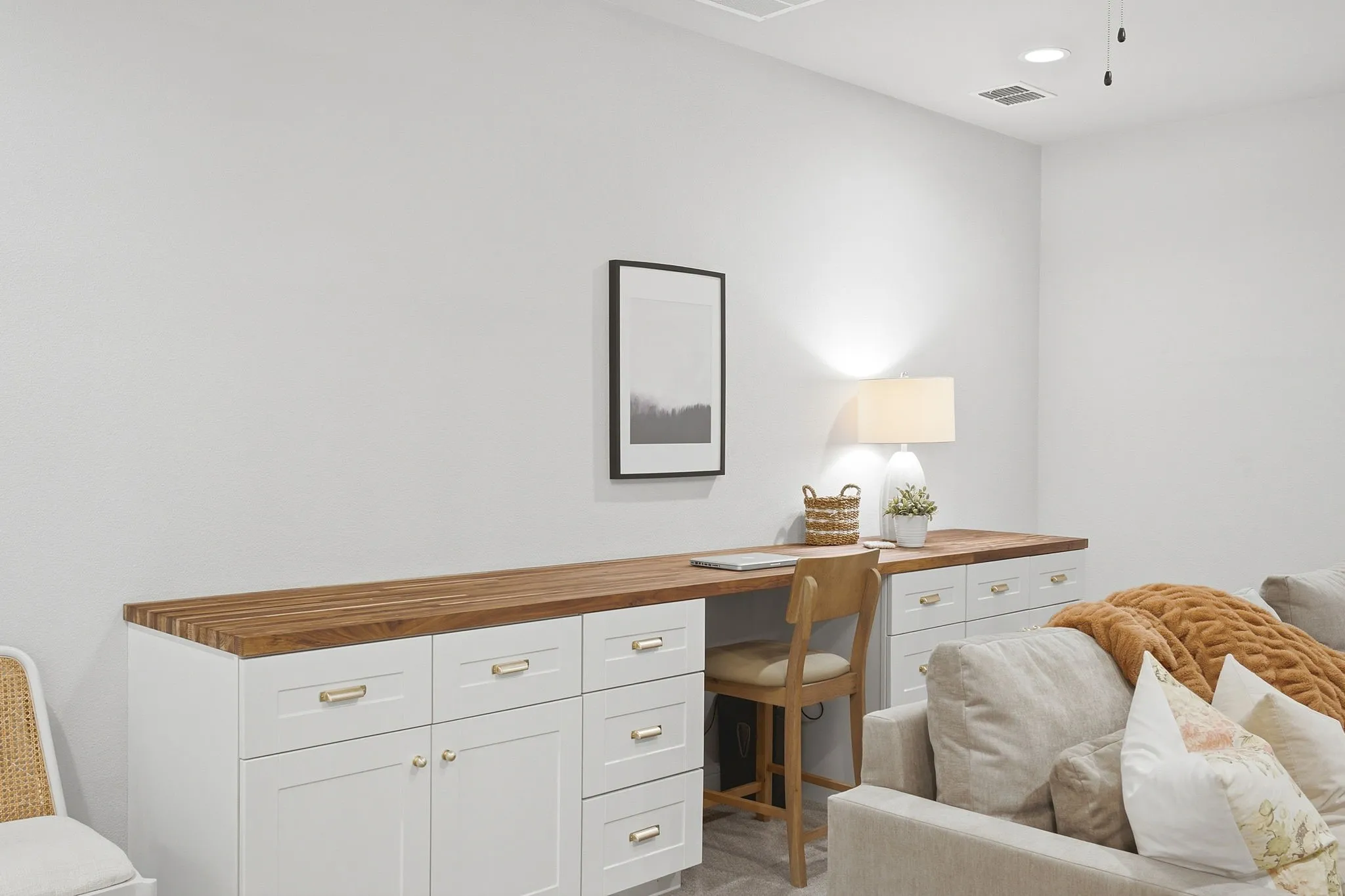 Built-in desk area with wood-finish countertop, white cabinetry with gold-tone hardware, and recessed lighting