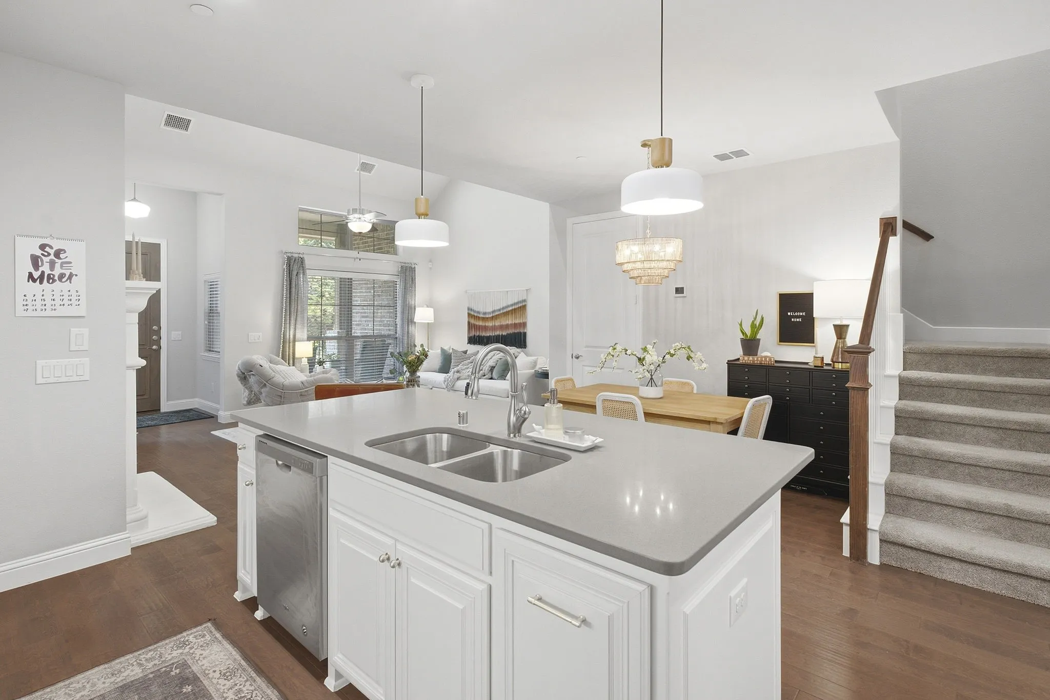Kitchen island with double sink and stainless steel dishwasher, vaulted ceiling, wood-finish flooring, and carpeted staircase